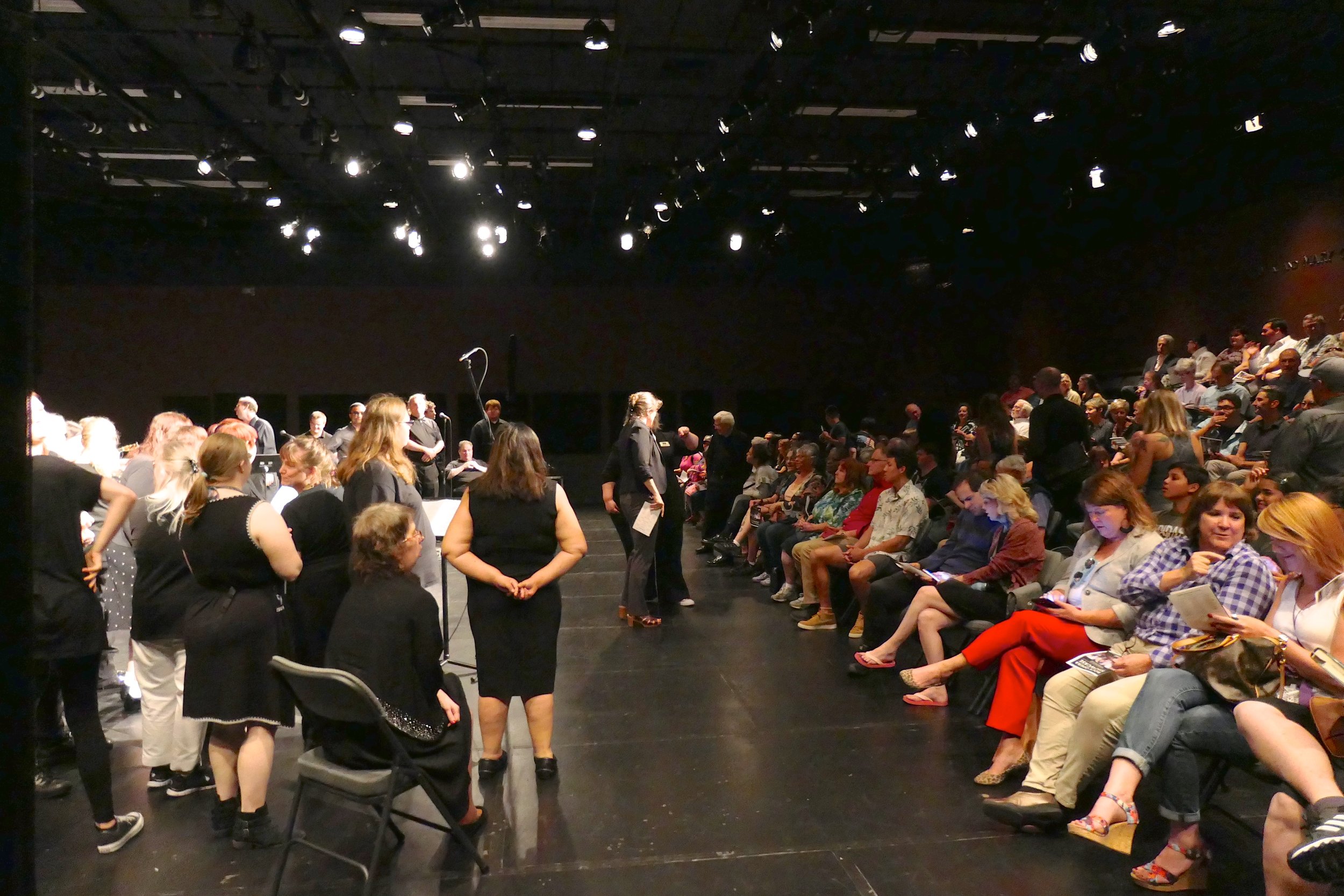 Performers and seated audience in a black box theatre seen from the side