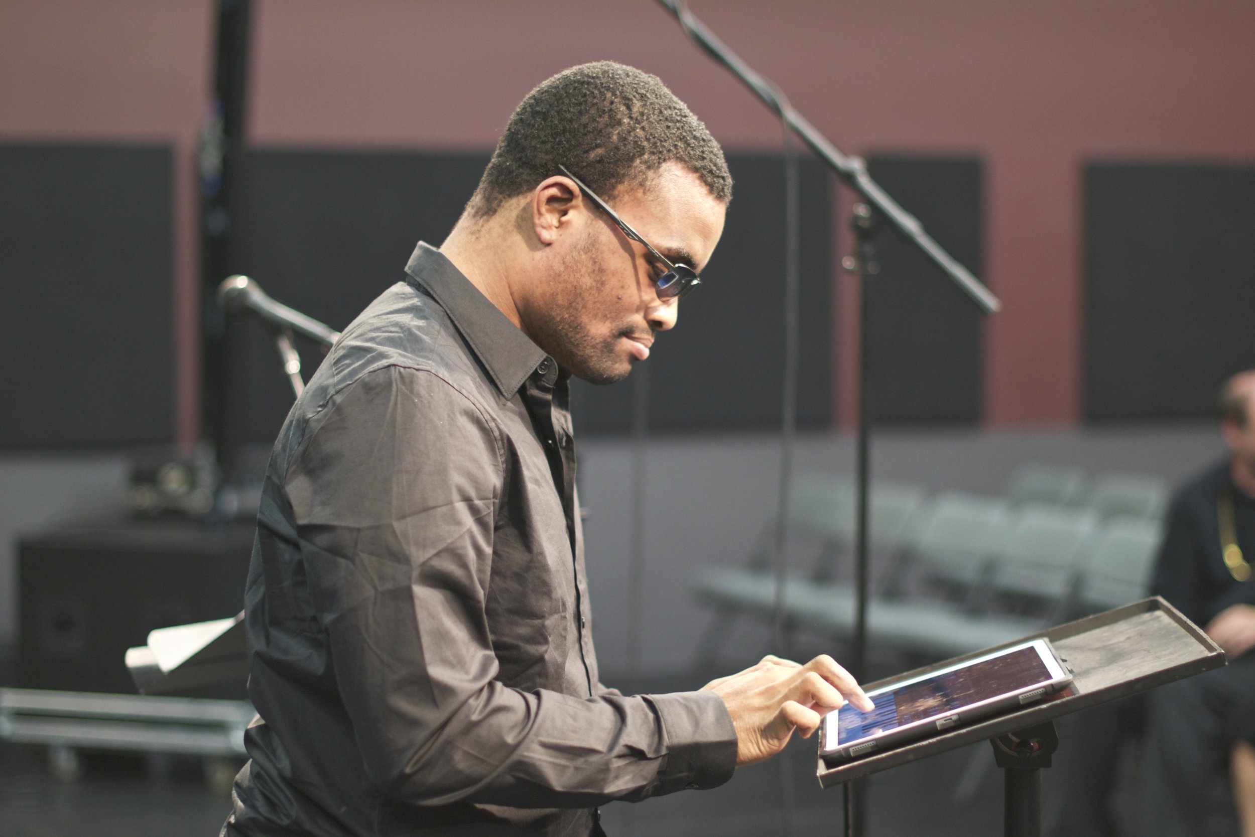 Man with dark glasses seen from the side, touching an ipad which sits on a music stand