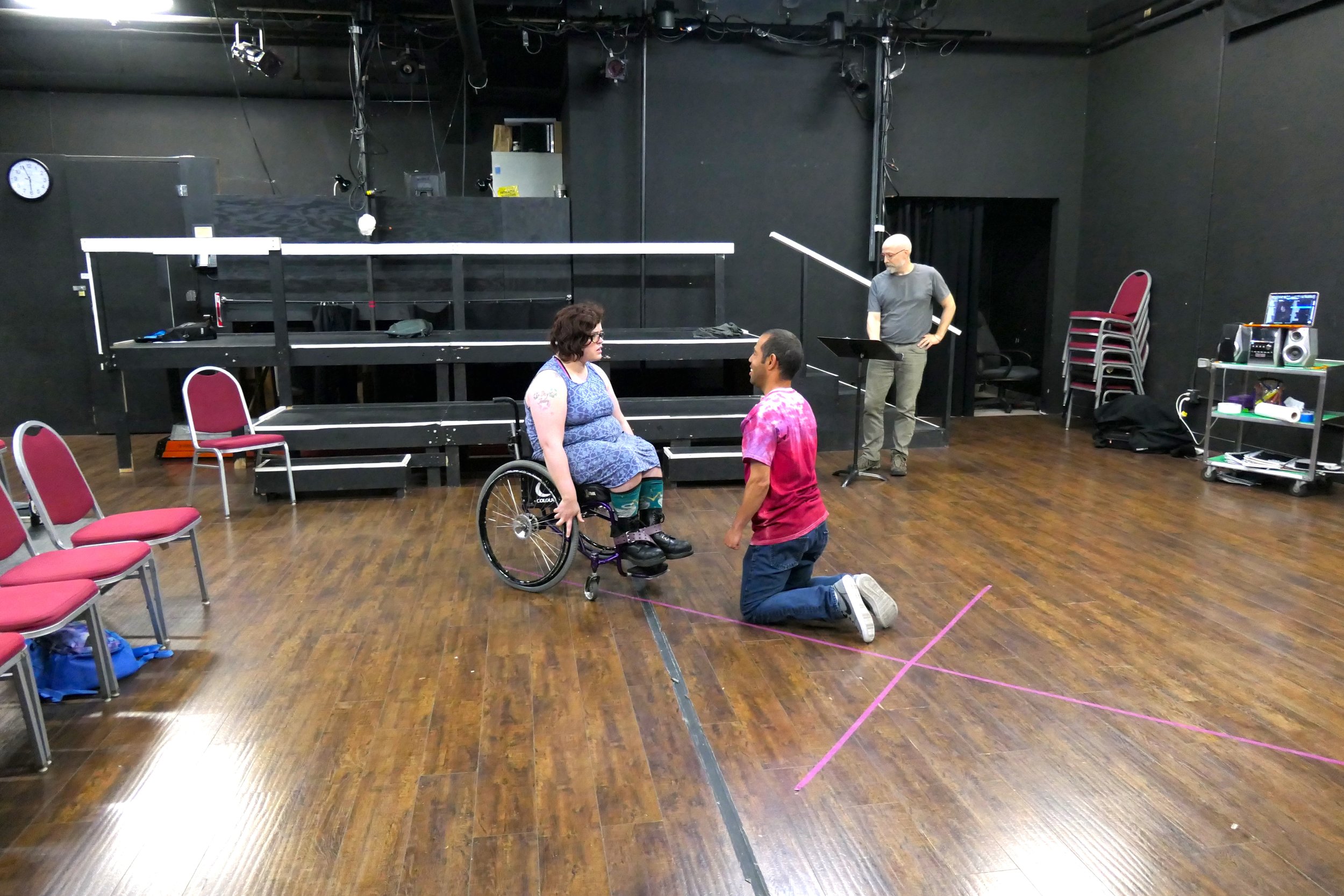 Three people in a black box theatre acting out a scene