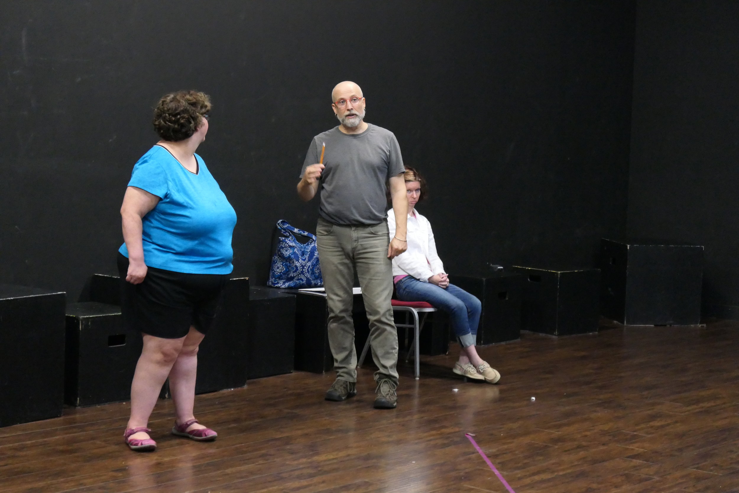 Three people in a black box theatre acting out a scene