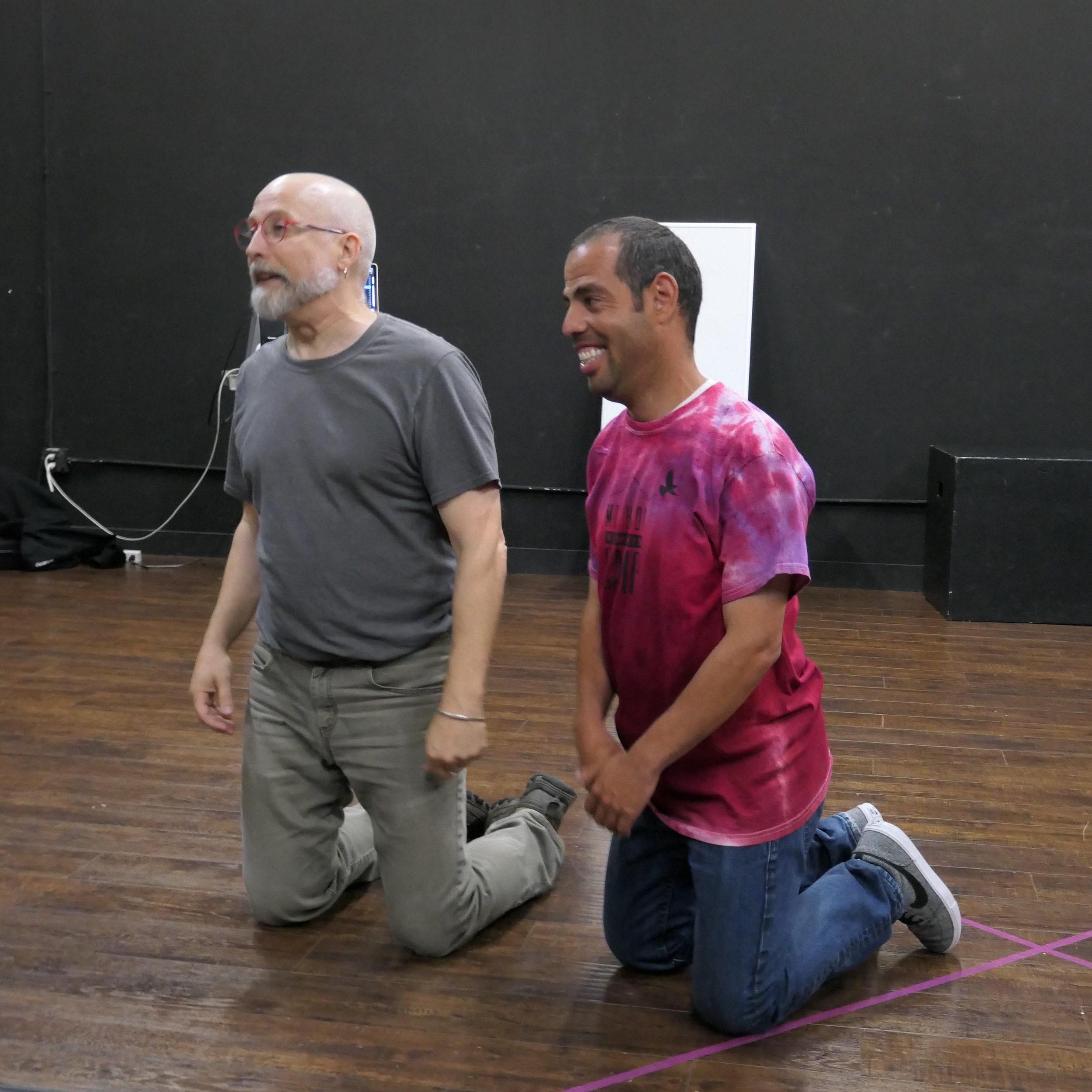 Two people kneeling in a black box theatre
