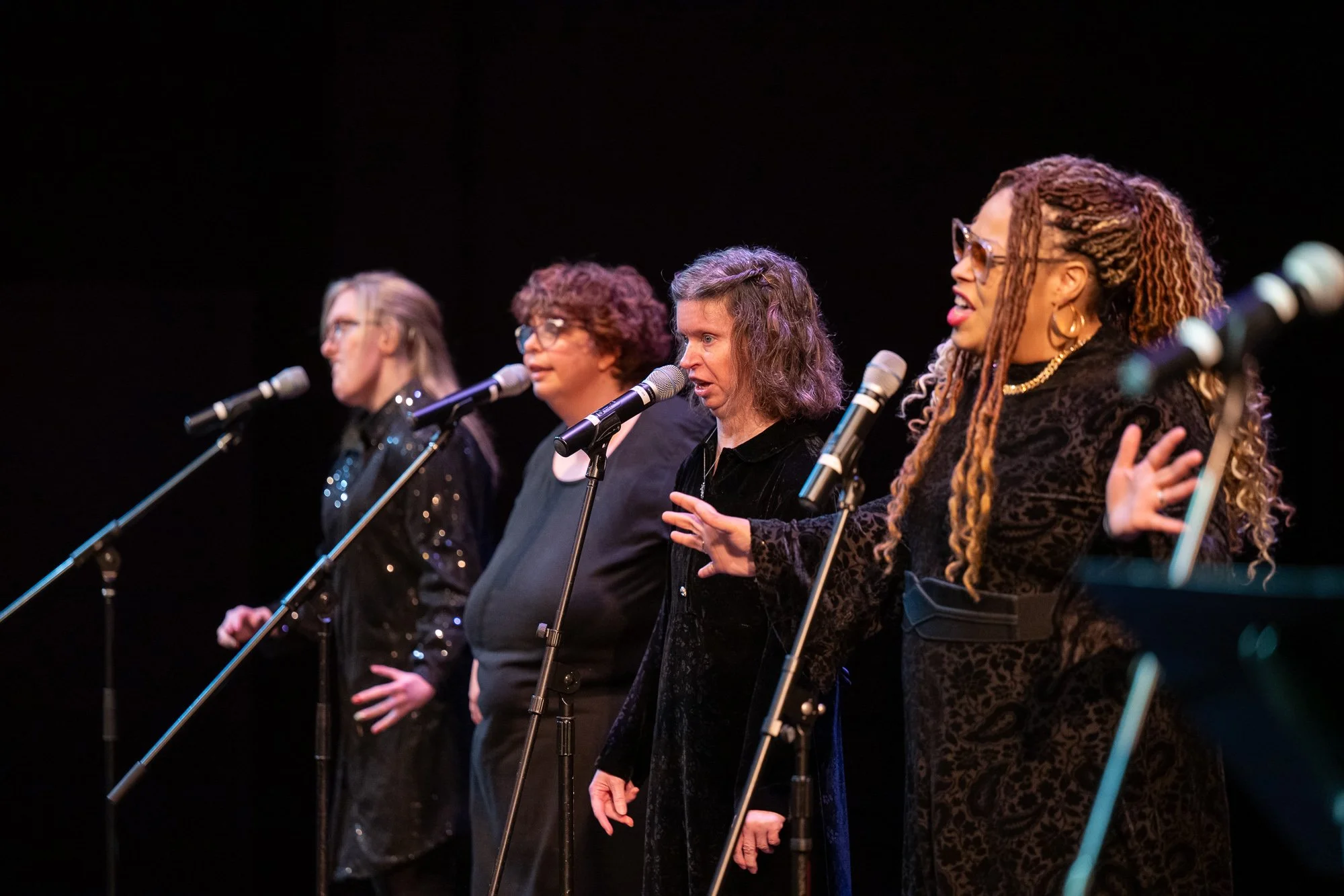 Four queens, dressed in black with a black background