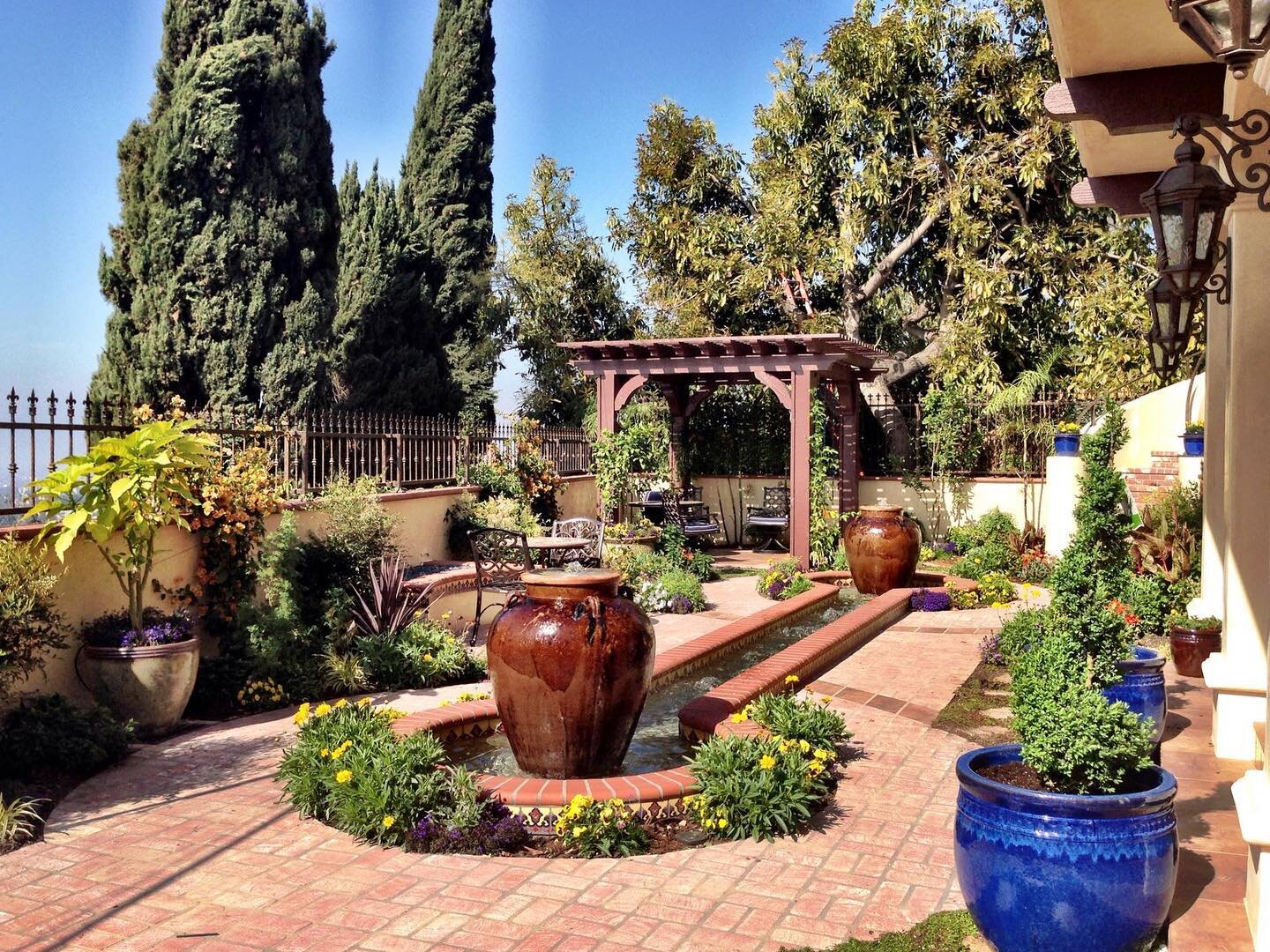 Bringing some bright colors and good vibes to your week with this Spanish style stunner! 🤩⁣
The water feature with large urns is set to run during the day and is dramatic when lit at night. The pergola provides a shady corner to relax and the small 