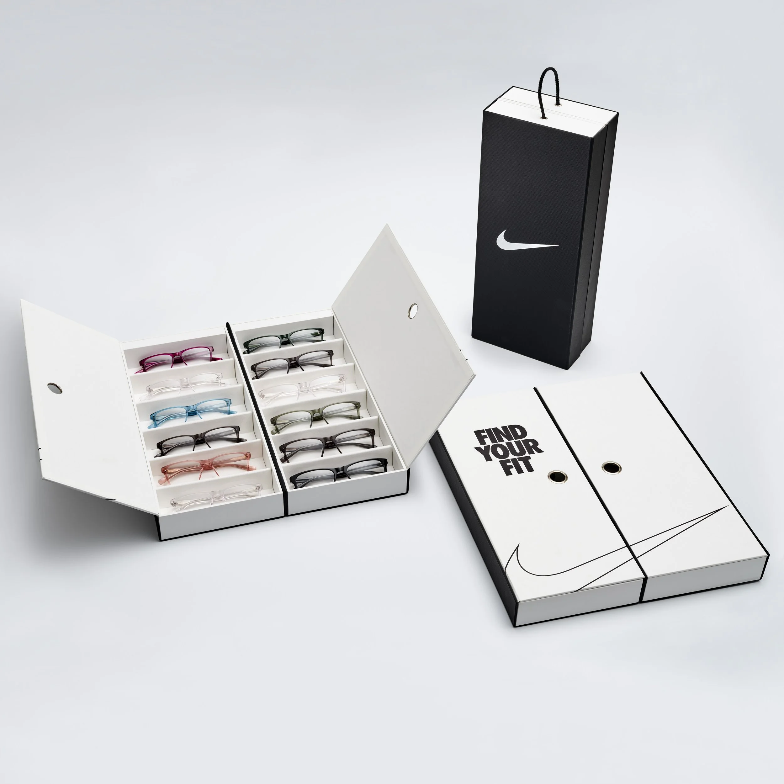 A display of eyeglasses in a white box with compartments, and a black box with a Nike logo, on a white surface.