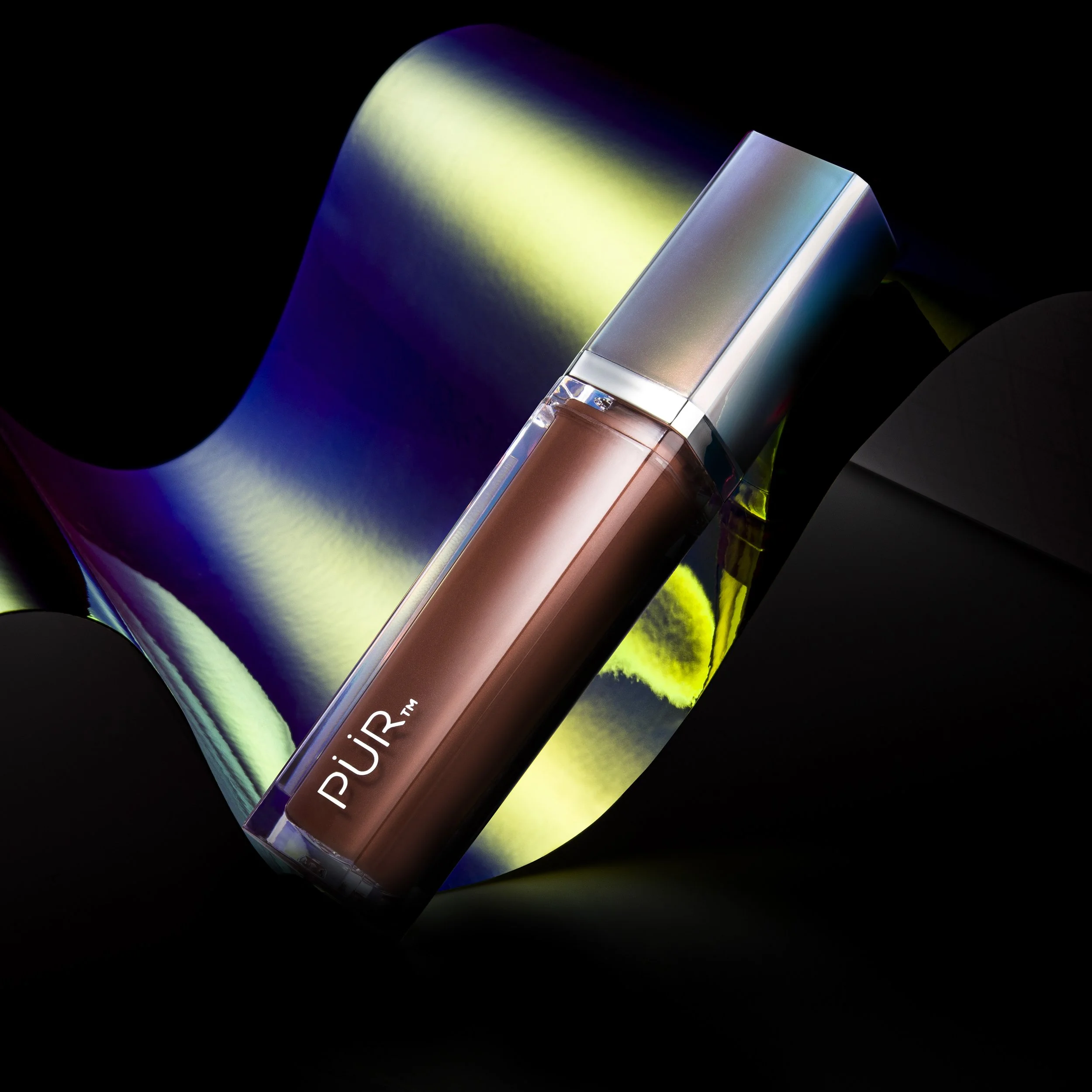 Cosmetic product called PUR lip gloss or lipstick with metallic packaging, positioned against a shiny, colorful background.