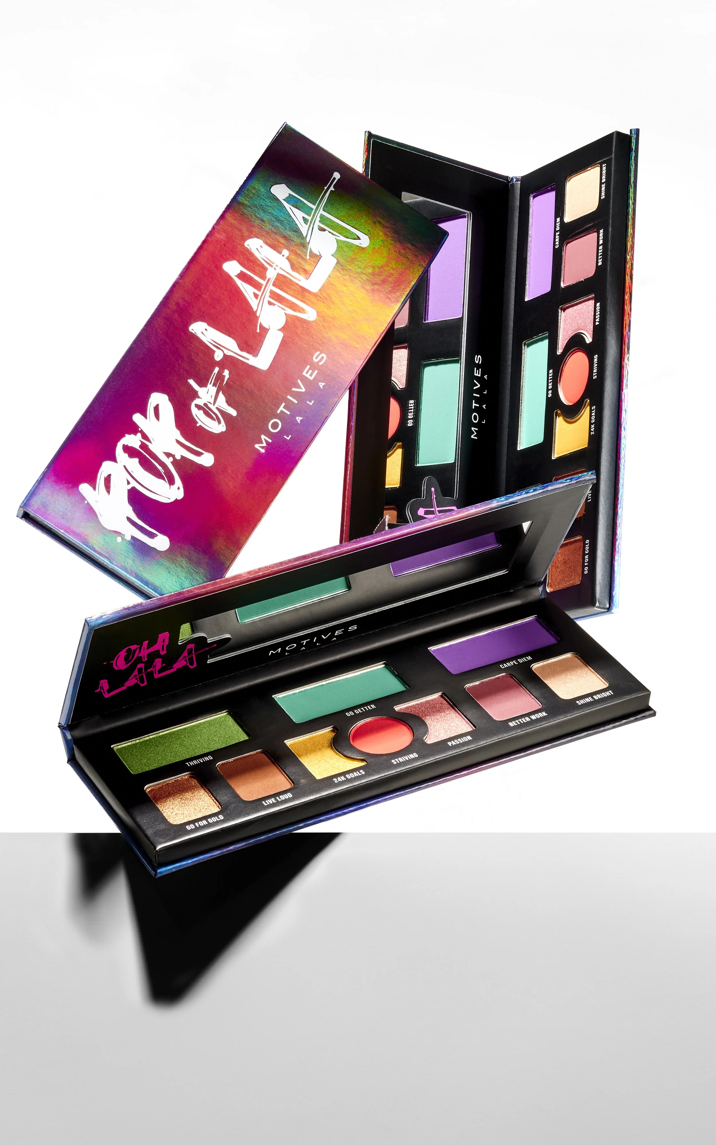 Open colorful makeup palette with various eyeshadows, blushes, and highlighters, placed on a white and black surface.