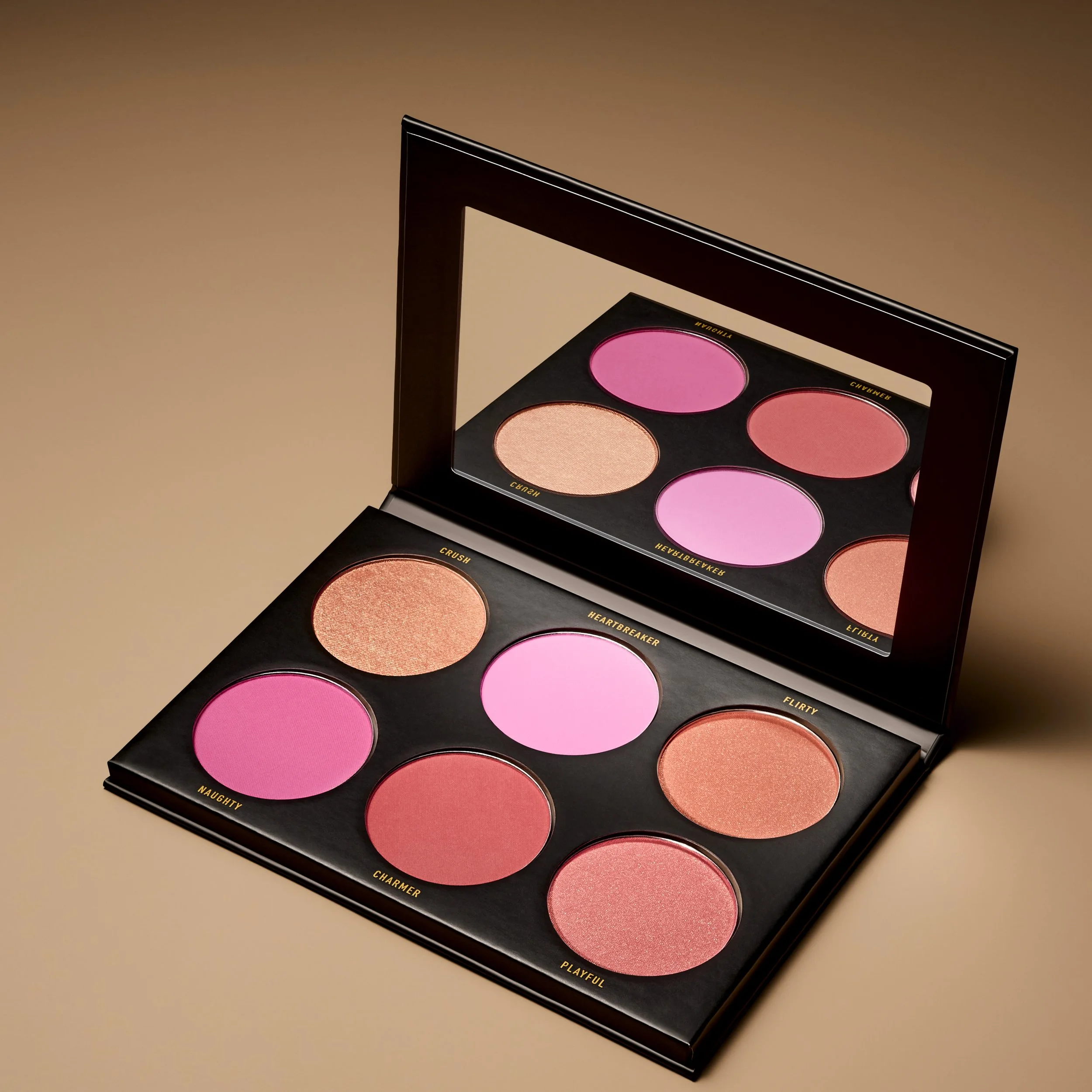 Open makeup palette with six blush shades, including pinks and peaches, in a black case with a mirror.