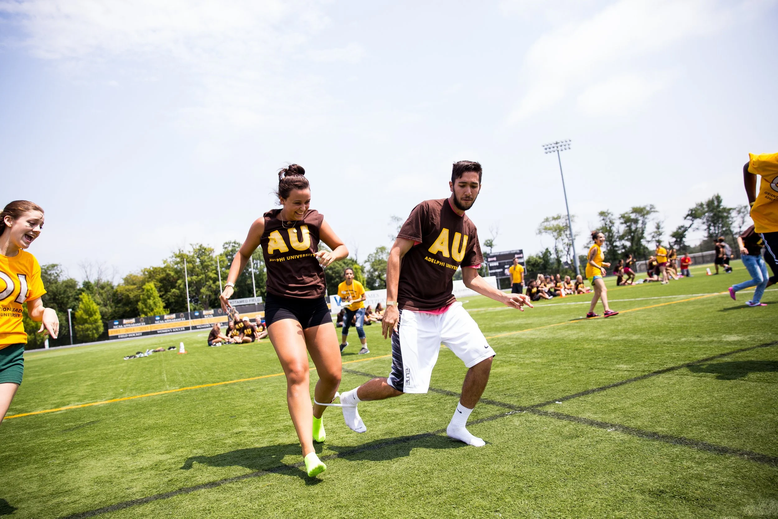 People participating in a tie-dye contest on a sunny day at Adelphi University on the football field.