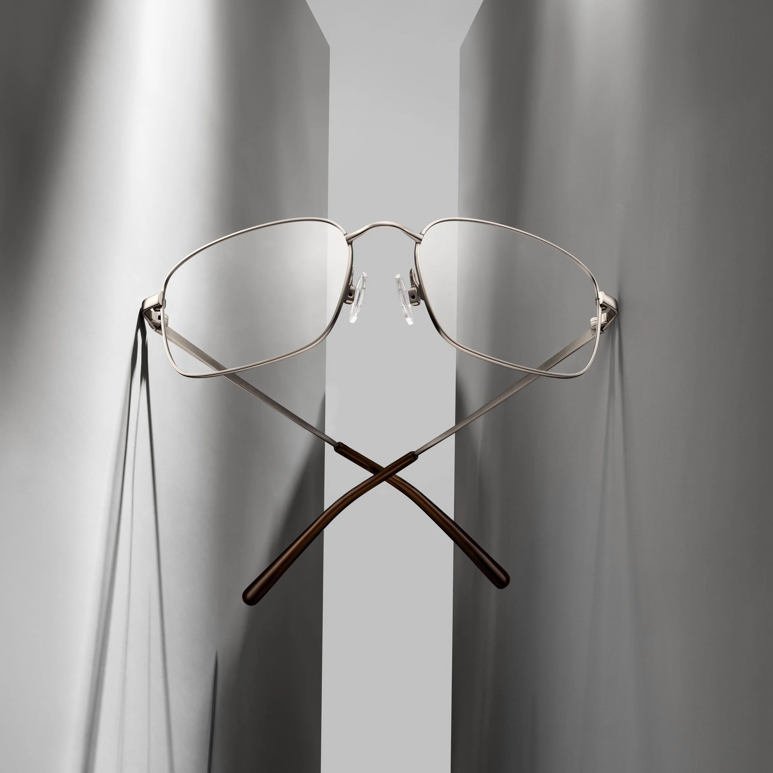 A pair of eyeglasses with a metal frame crossed and resting on a reflective gray surface.