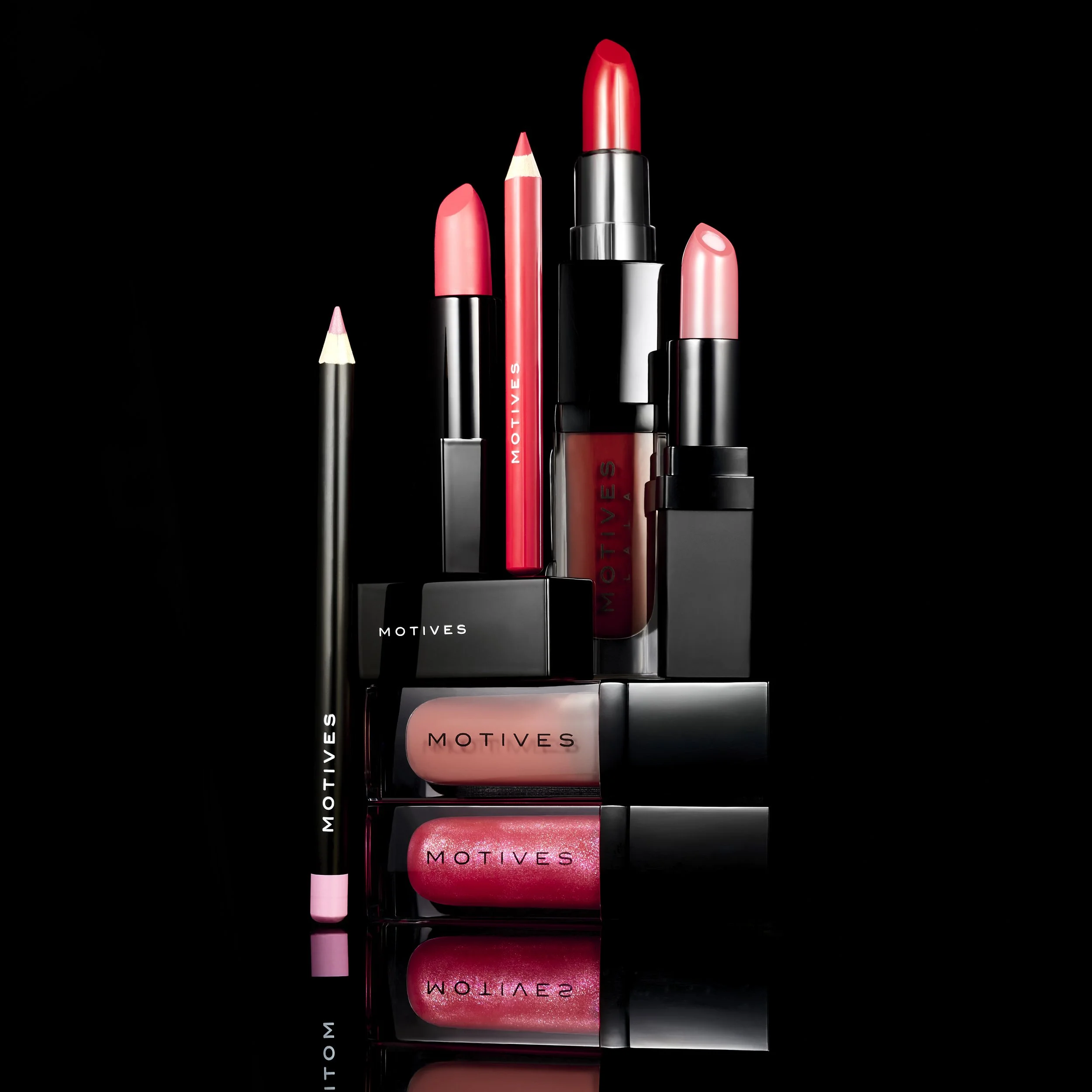 Collection of Motives makeup products including lipstick, lip gloss, lip liner, and lip crayons, arranged against a black background with reflections.