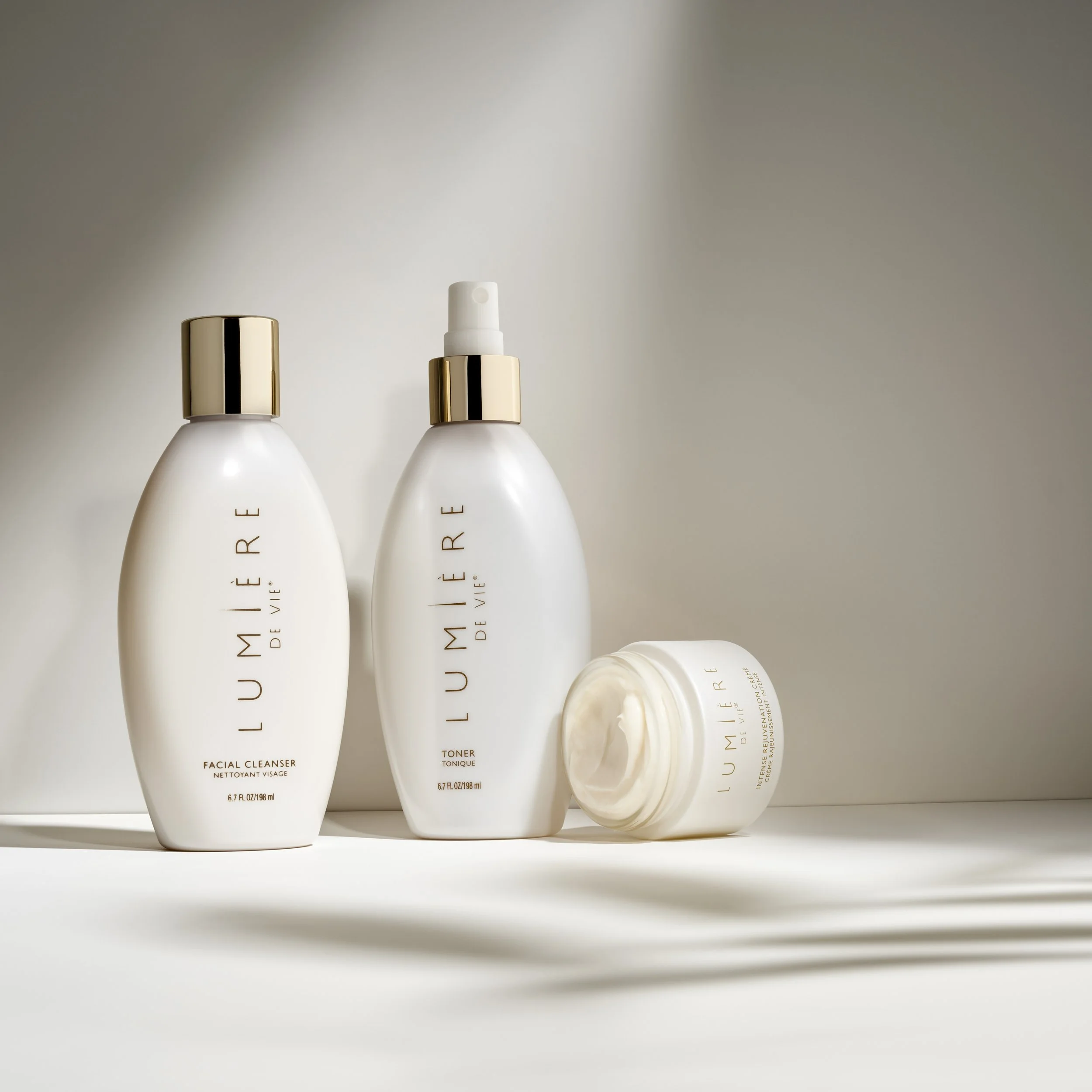 A collection of luxurious skincare products from Illuminé De Vie, including a facial cleanser, toner, and night cream, with sleek white bottles and gold accents, displayed on a white surface with a neutral background.