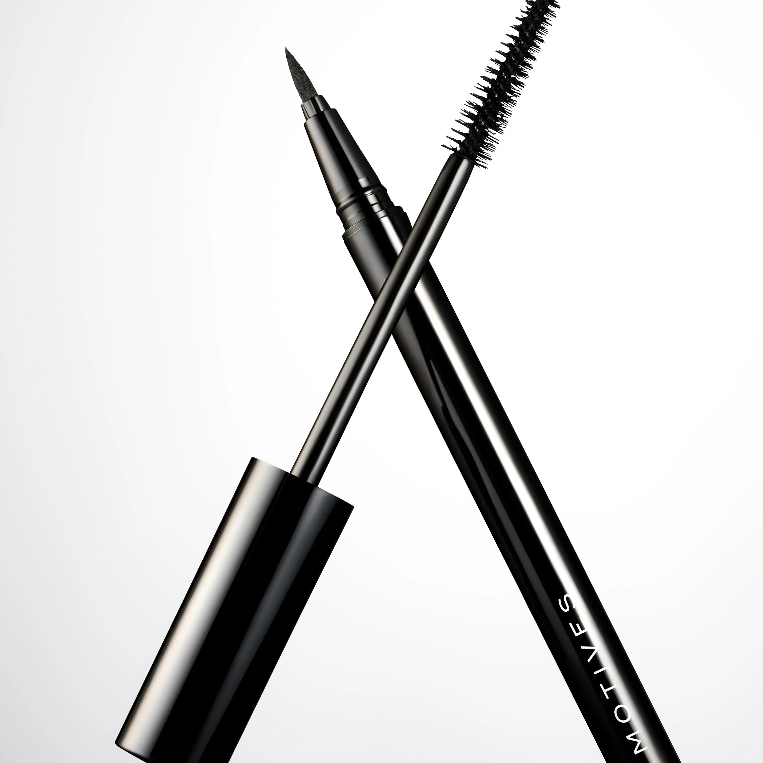 Close-up of a black liquid eyeliner pen with a fine tip and a spoolie brush, crossed against a white background.