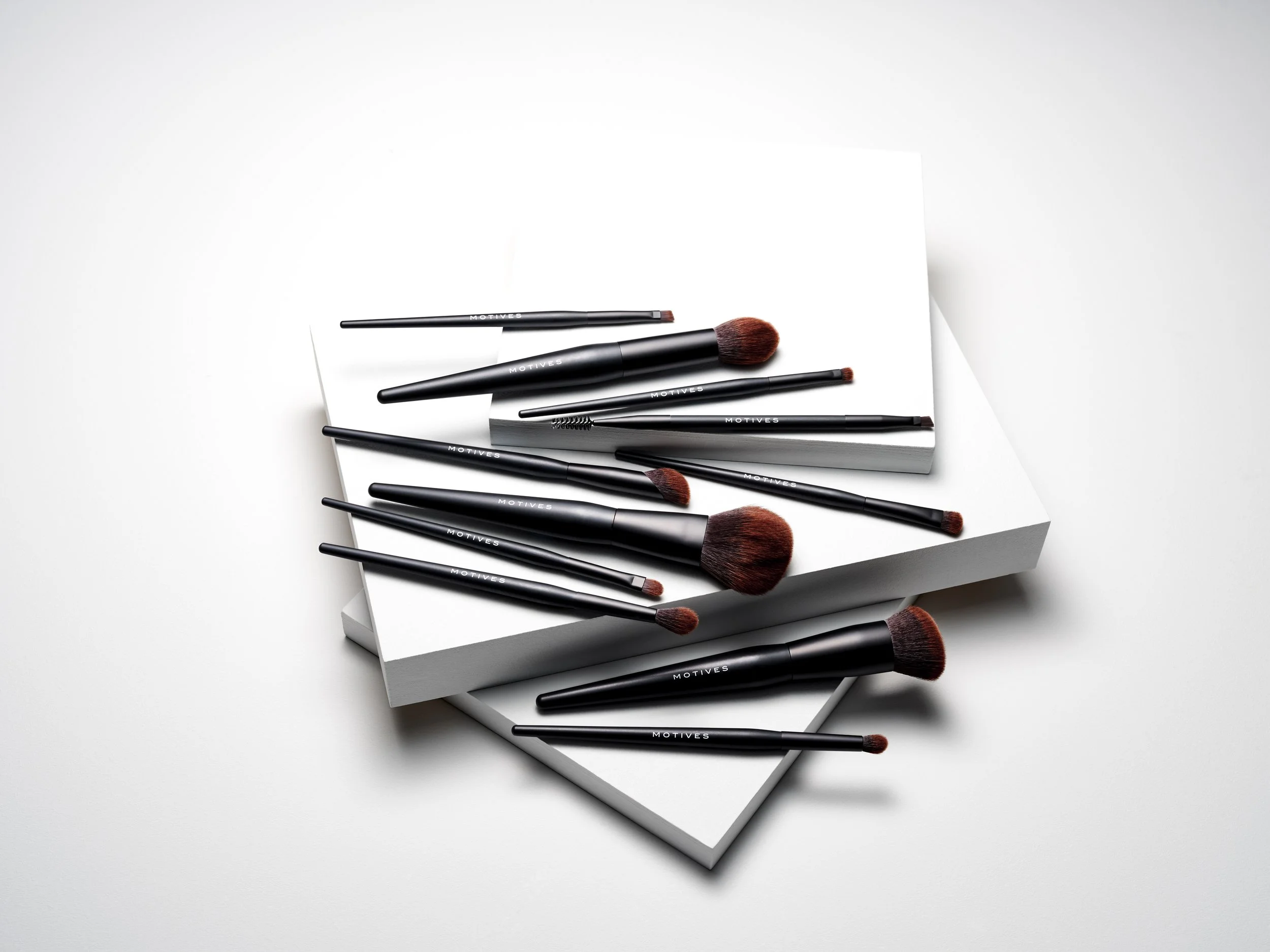 Set of black makeup brushes with brown bristles on top of white notebooks, arranged in a visual display.