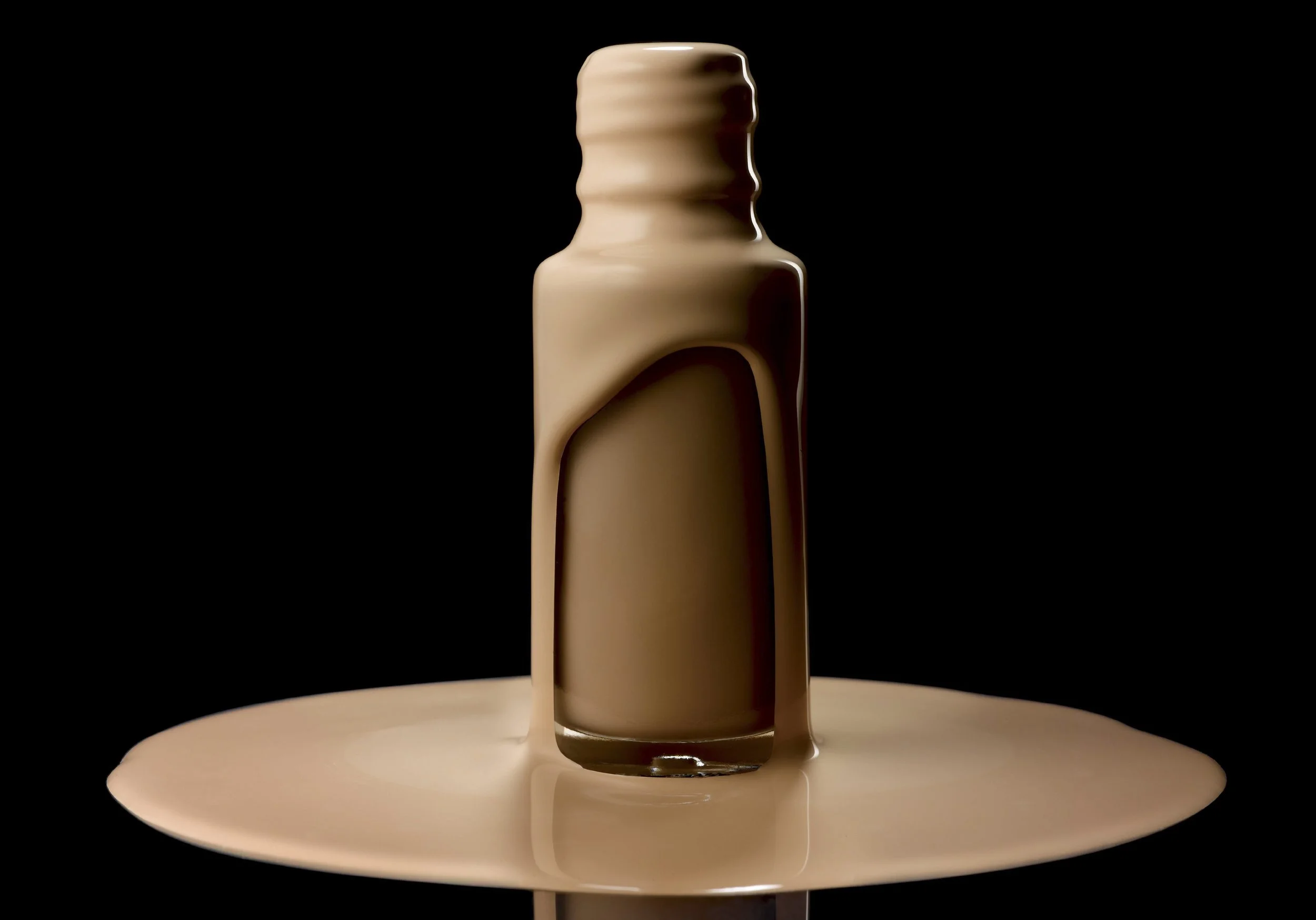 A bottle of chocolate sauce with some sauce spilling over and pooling on a flat surface, set against a black background.