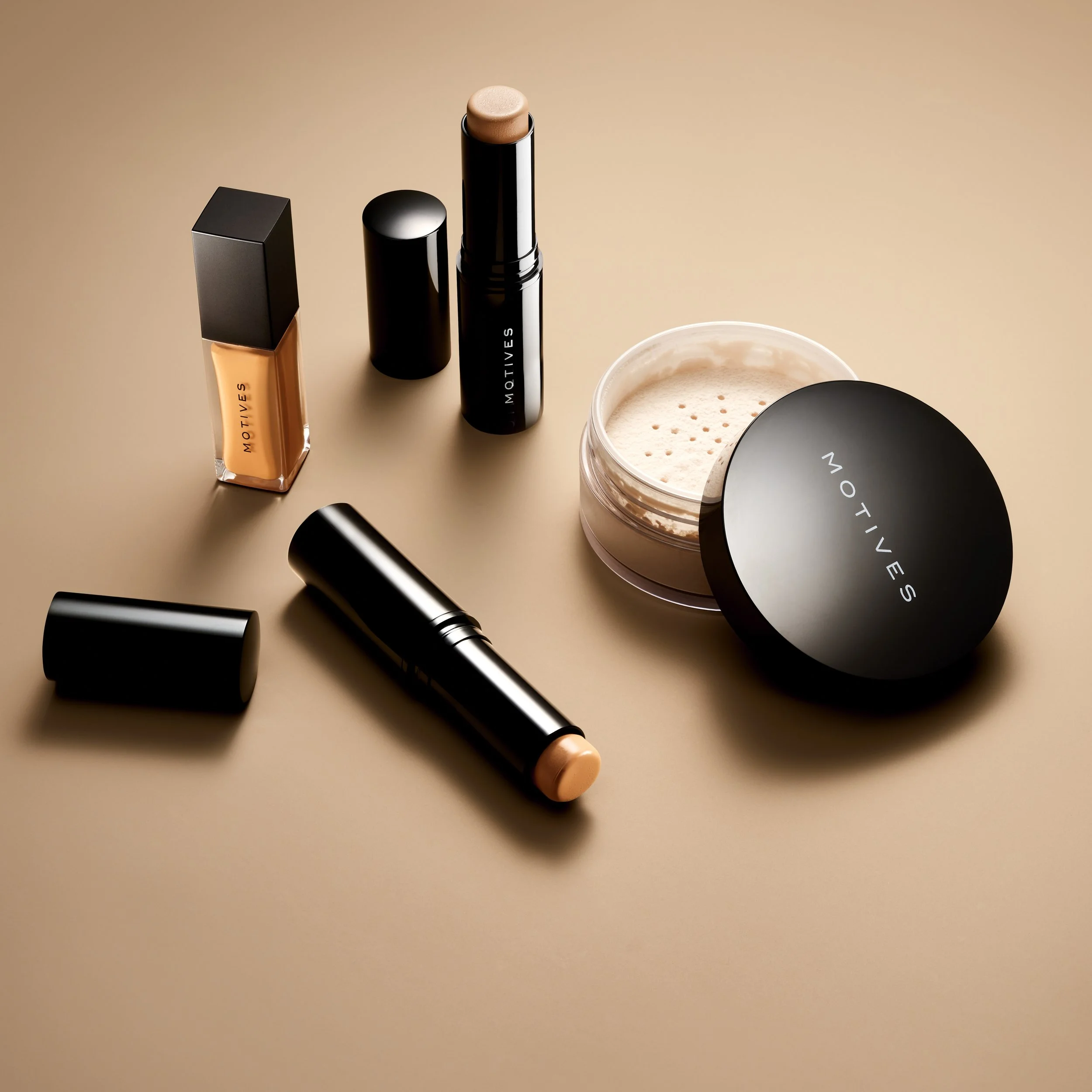 Collection of MOTIVES makeup products, including foundation, lipsticks, and loose powder on a beige surface.