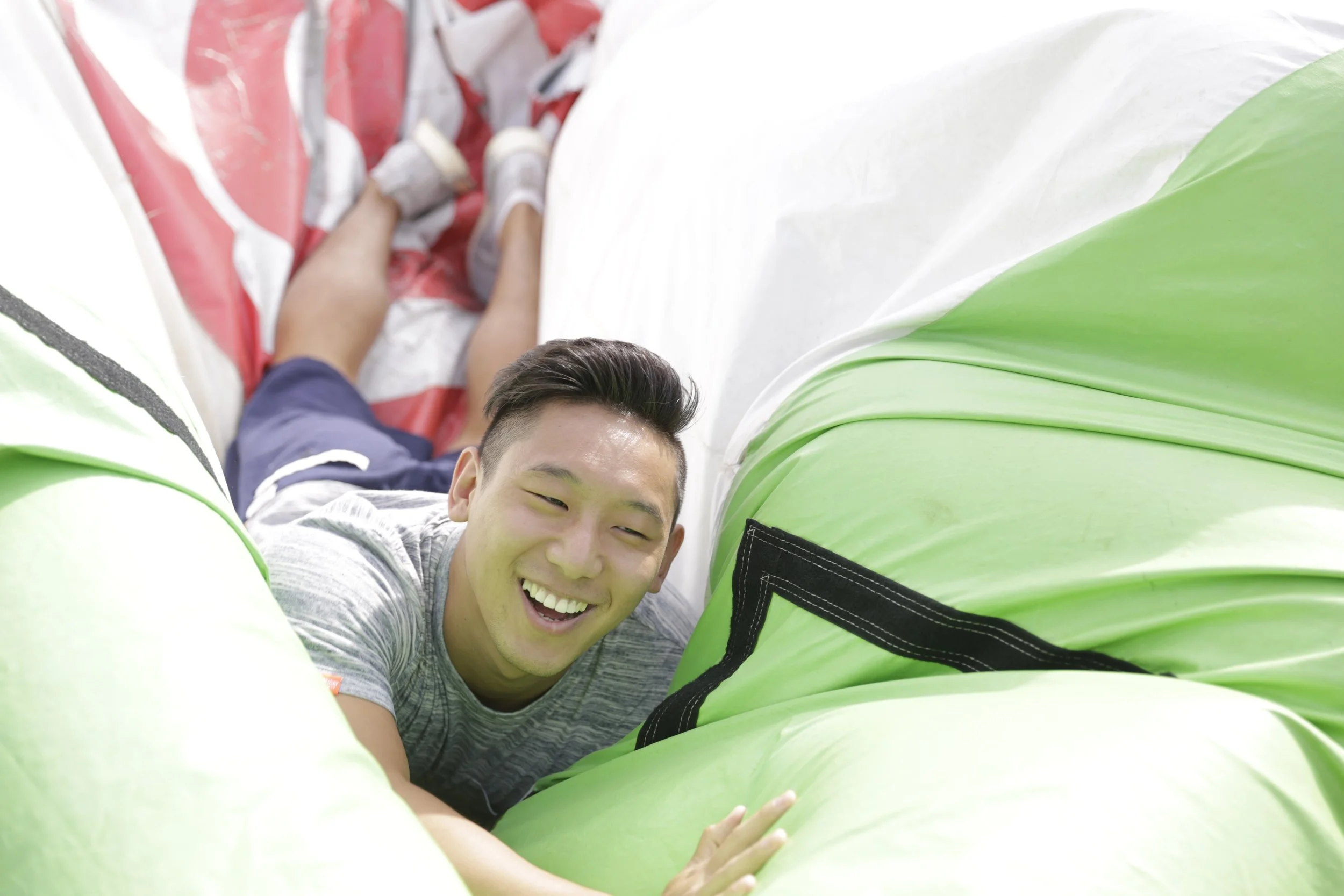 Young man smiling and crawling through an inflatable obstacle course or bounce house with green, red, and white sections.