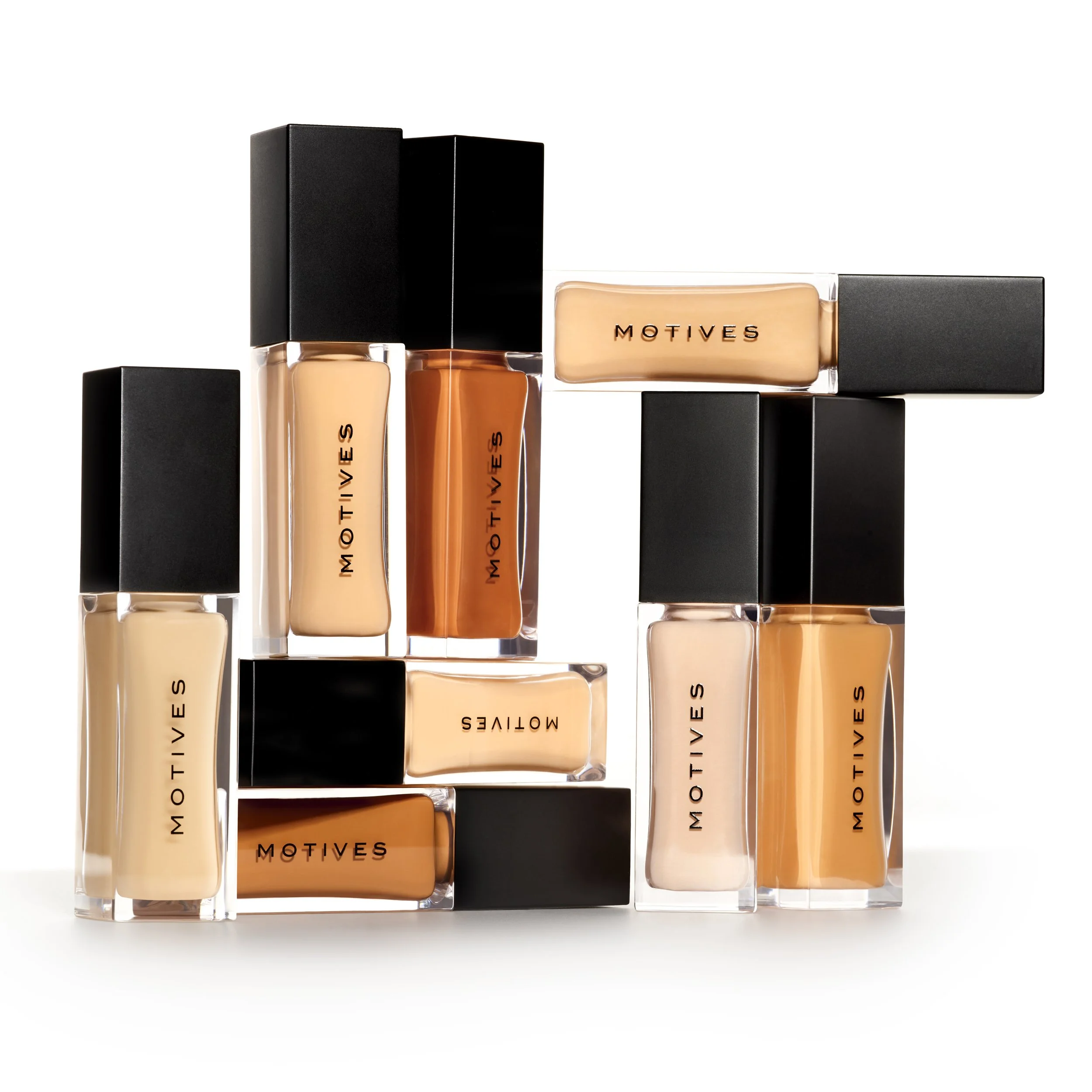 Collection of MOTIVES liquid foundation bottles with black caps arranged in a creative geometric pattern on a white background.