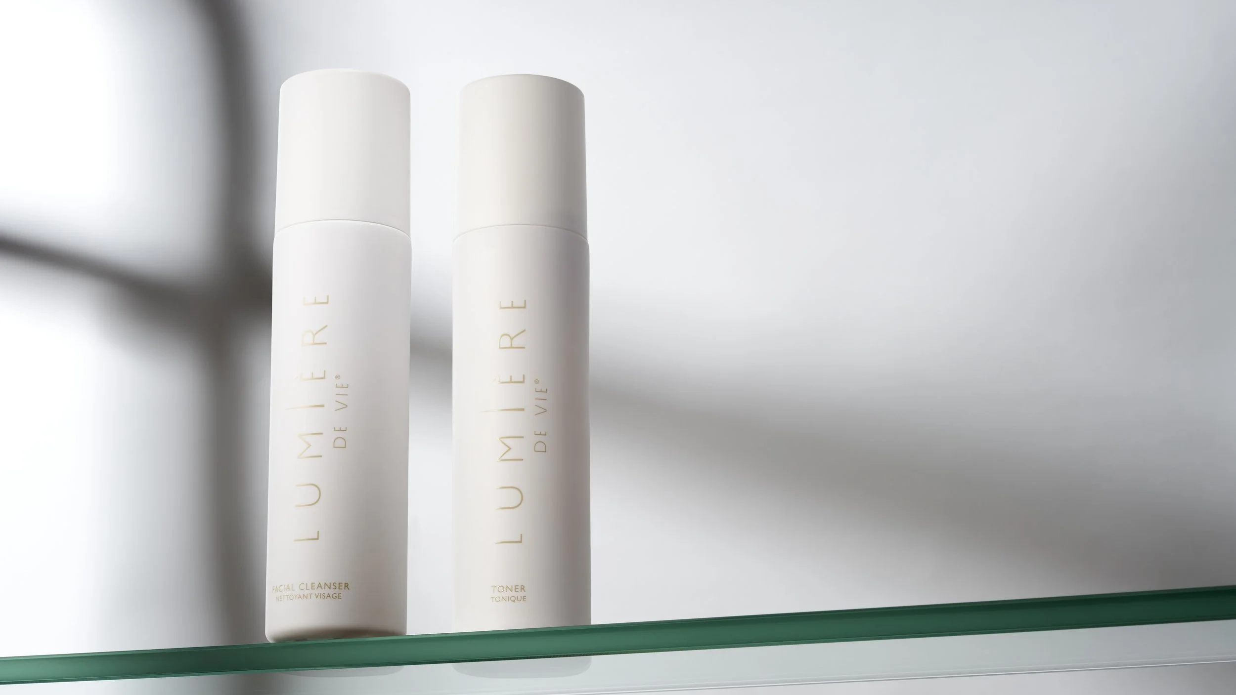 Two white cylindrical bottles labeled 'LUMIÈRE DE VIE', standing on a glass shelf with a white background.