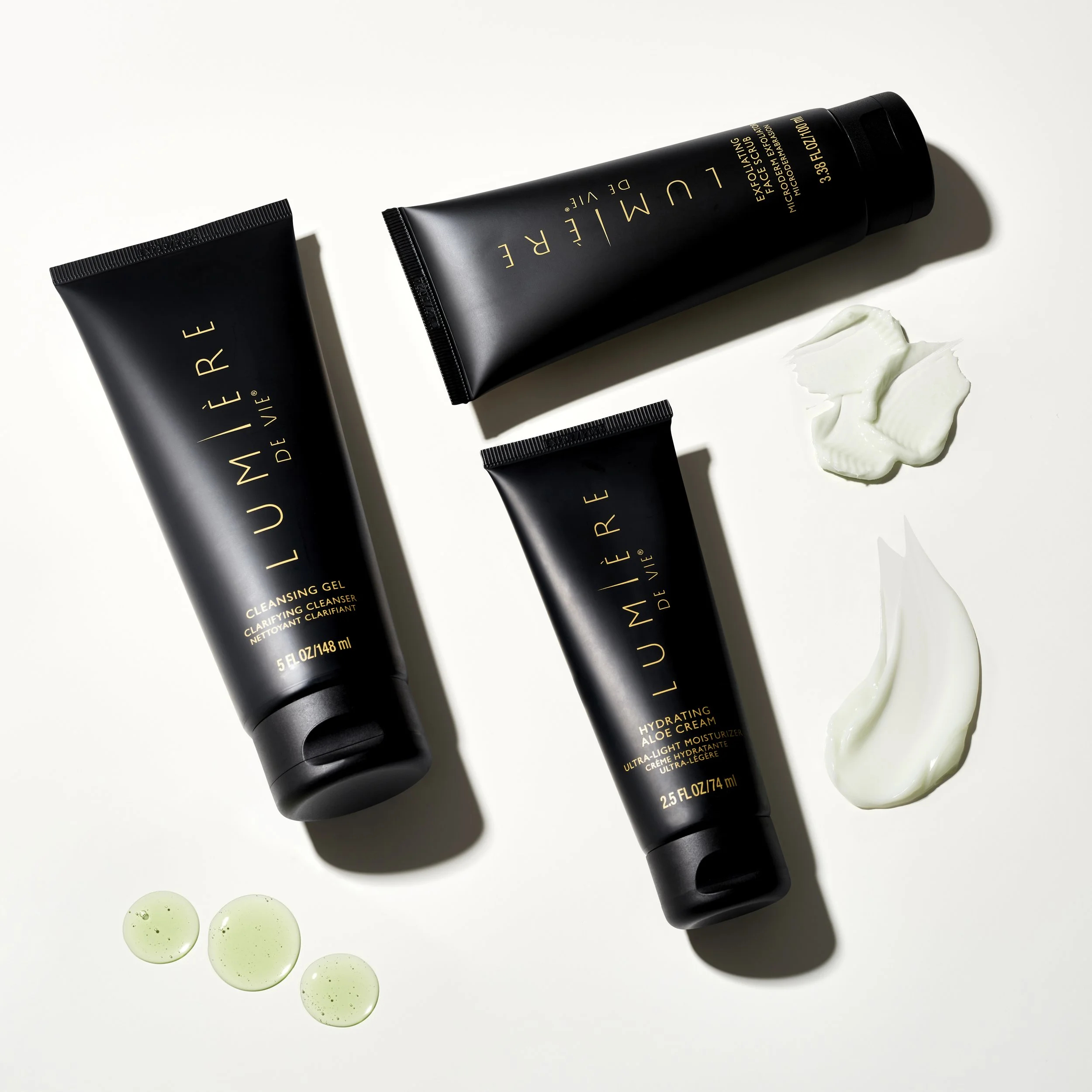 Black skincare tubes labeled "LUMIÈRE" with golden text, placed on a white background with dollops of cream and drops of green gel.
