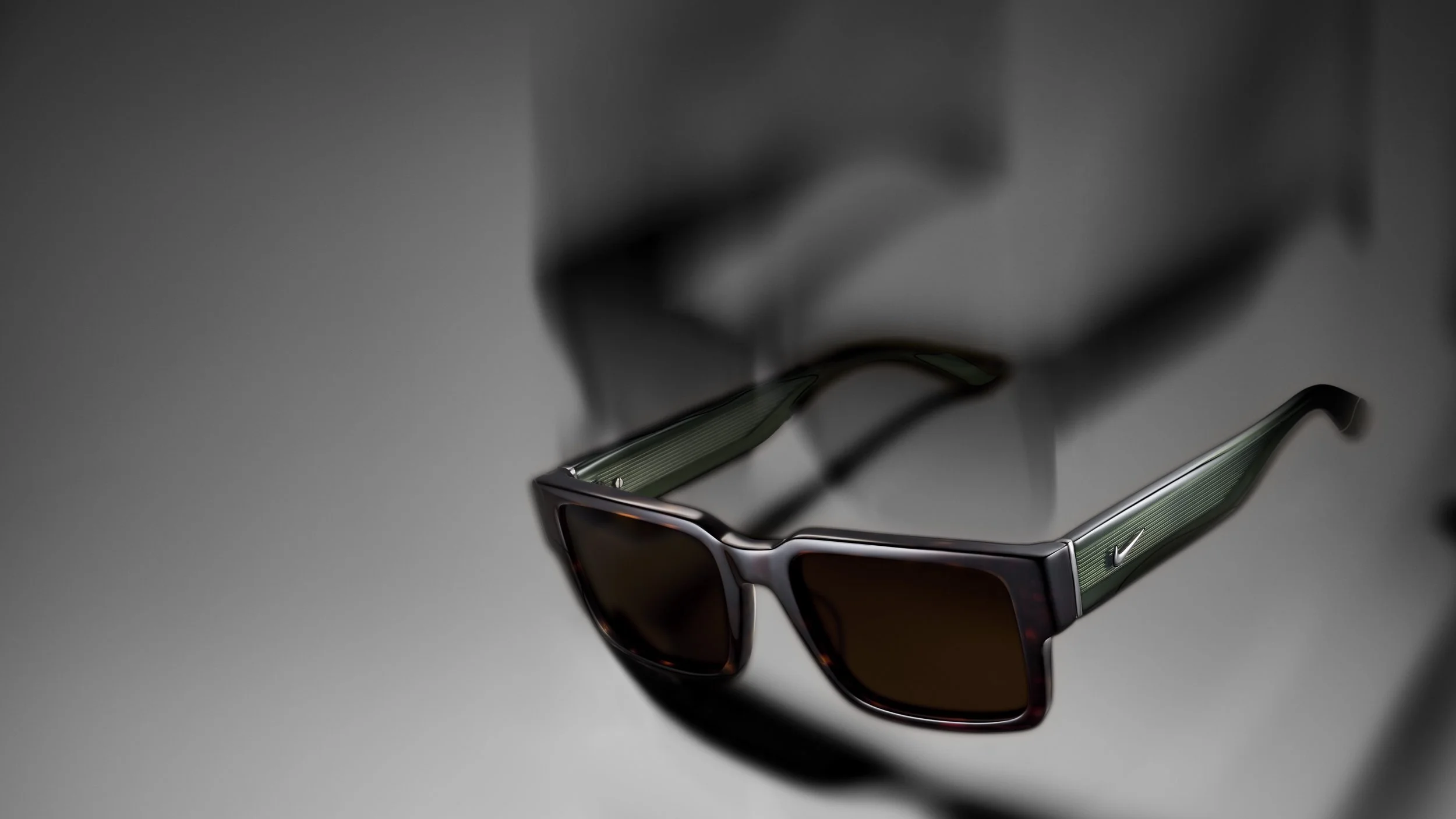 A pair of sunglasses with dark lenses and a silver frame, lying on a smooth gray surface.