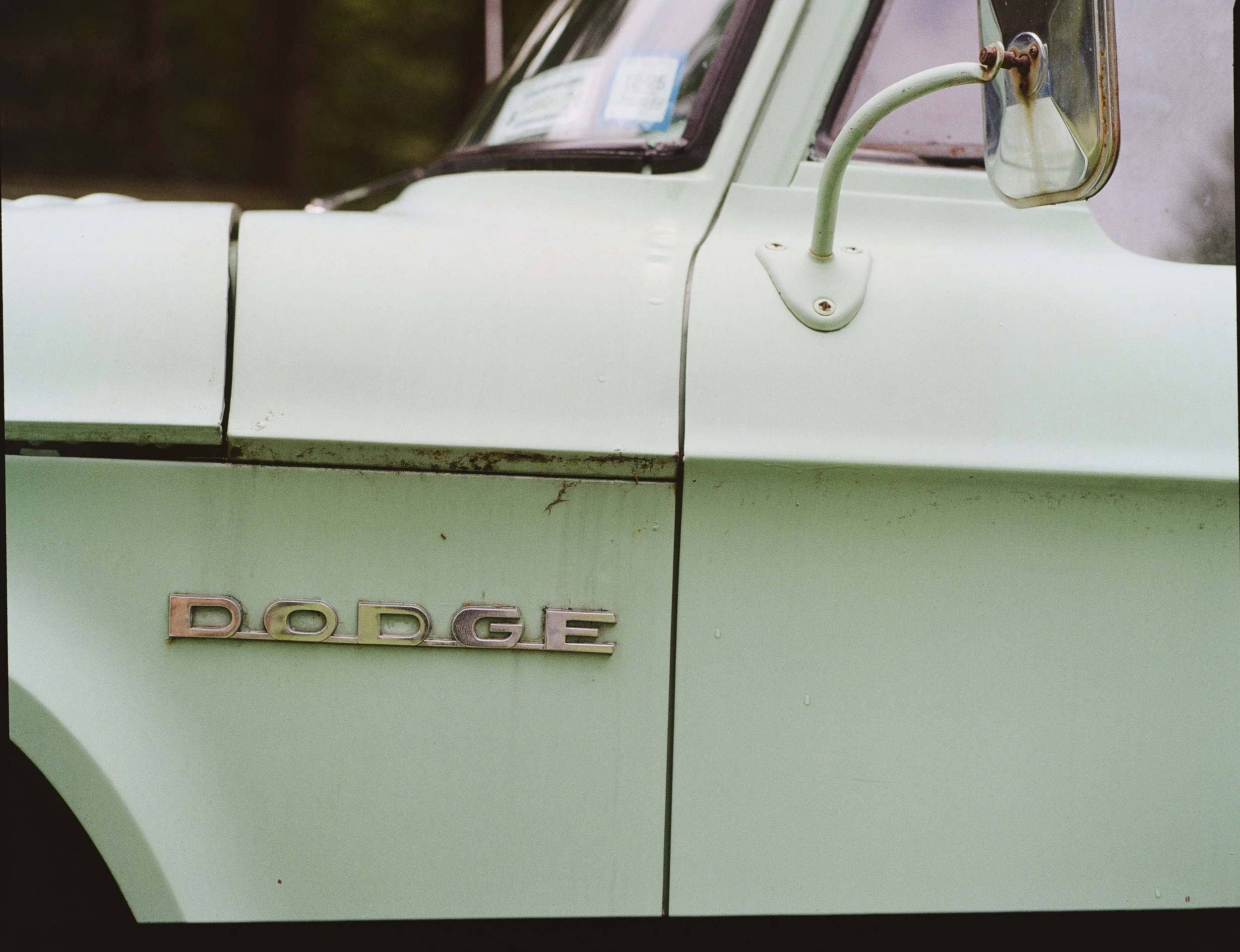 Close-up of a vintage light green Dodge truck's side view mirror and part of the door with a Dodge emblem.