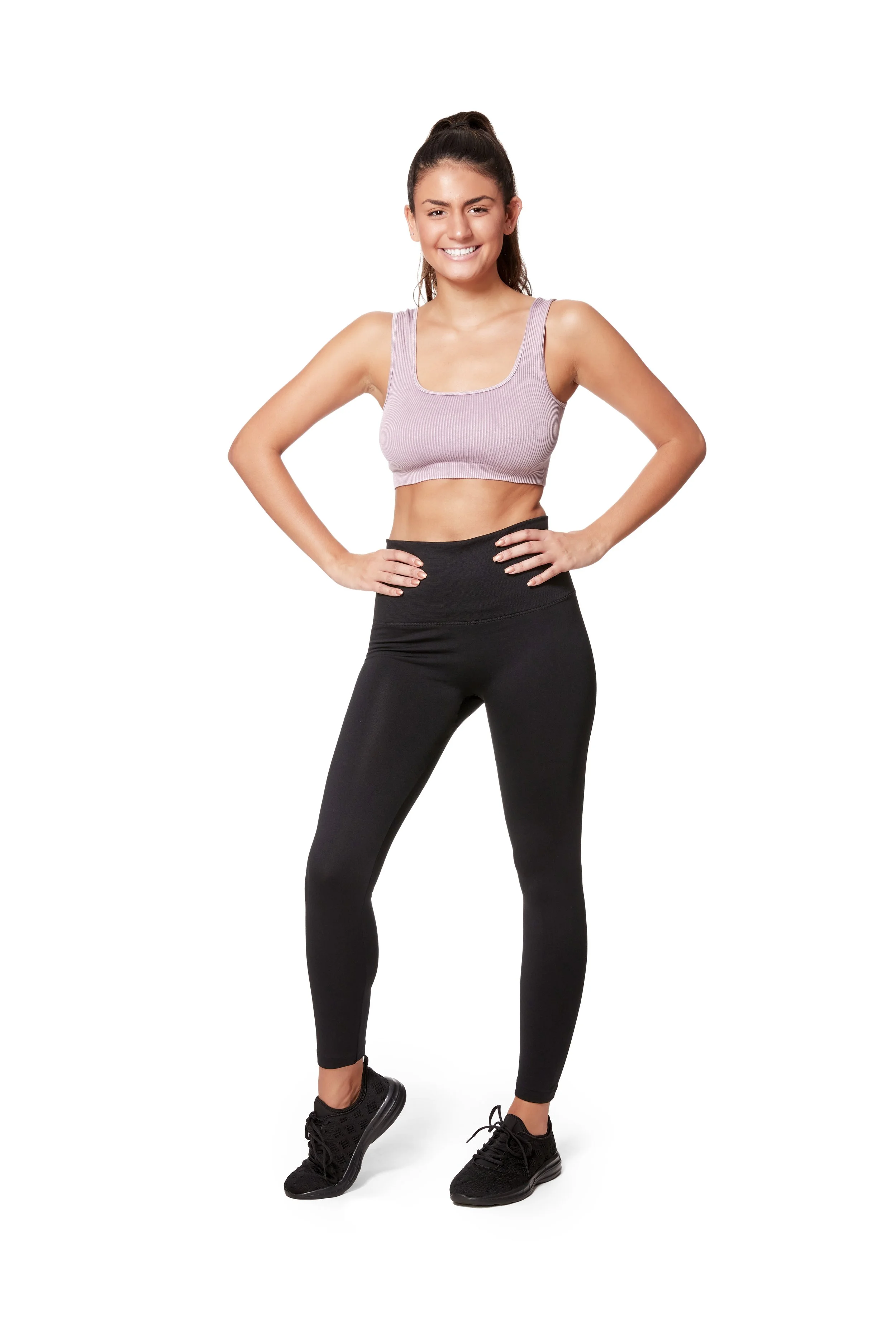 A young woman in athletic wear standing confidently with hands on hips and smiling.