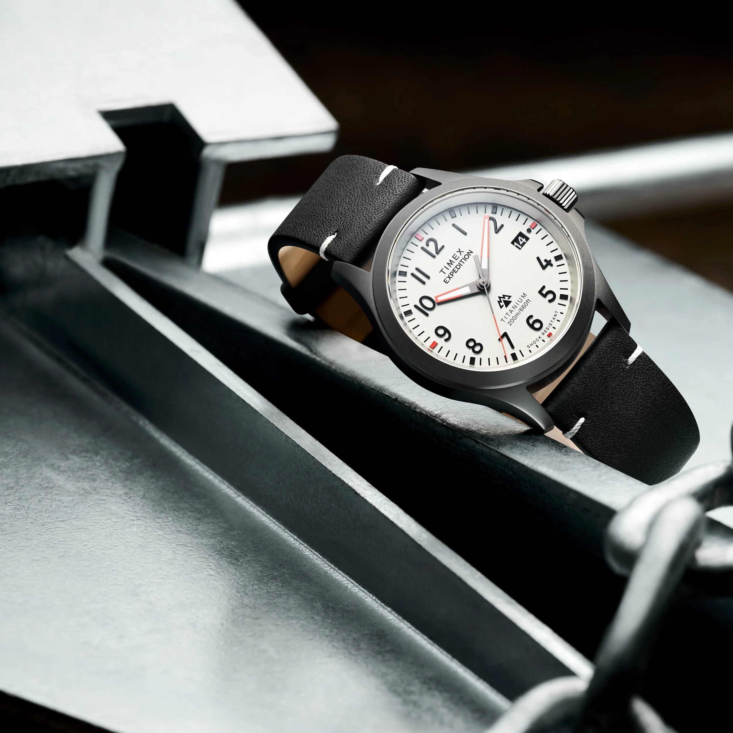 A Timex Expedition wristwatch with a black strap, white dial, black numerals, and red accents on a metal display stand.