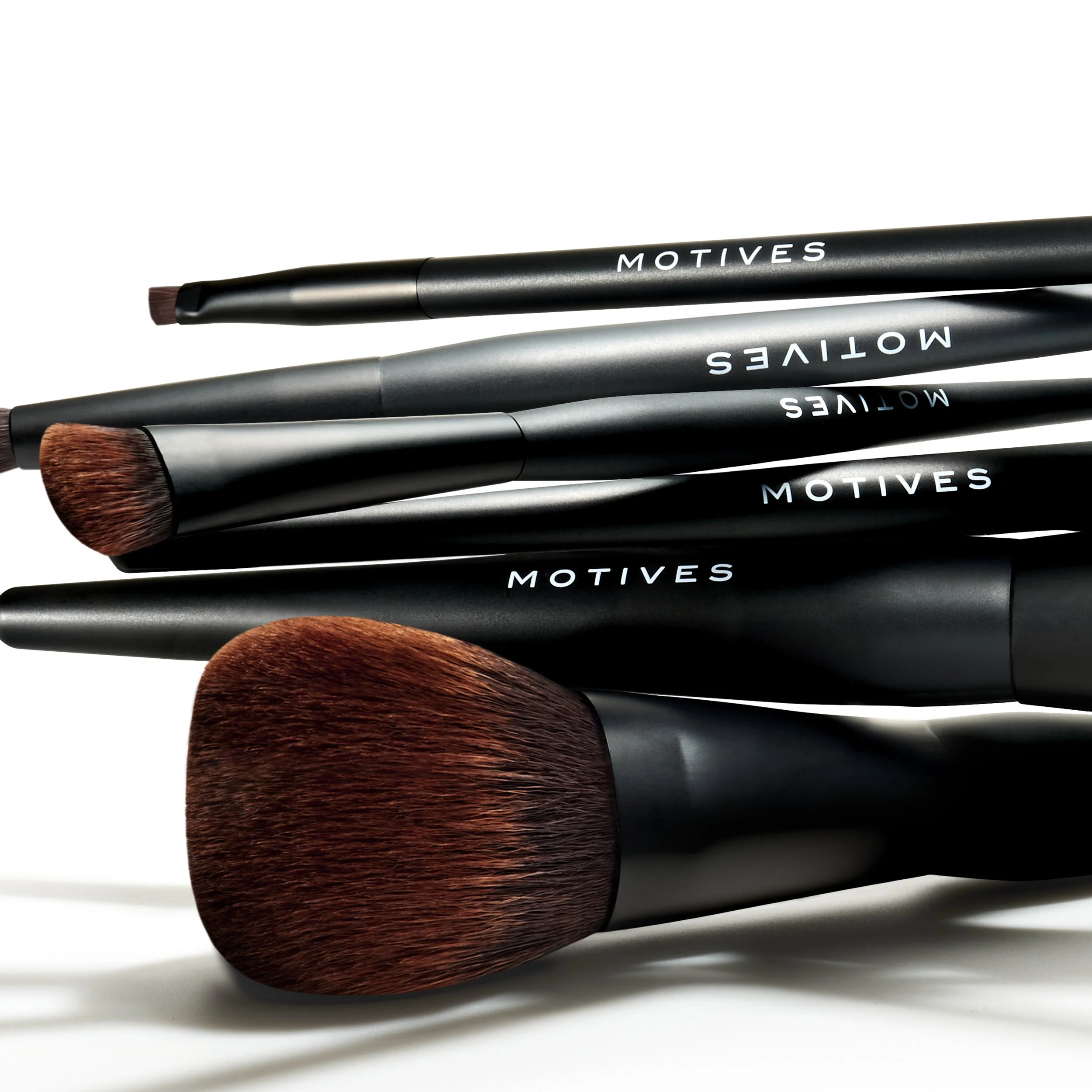 Set of black makeup brushes with brown bristles and white text reading 'MOTIVES' on a white background.