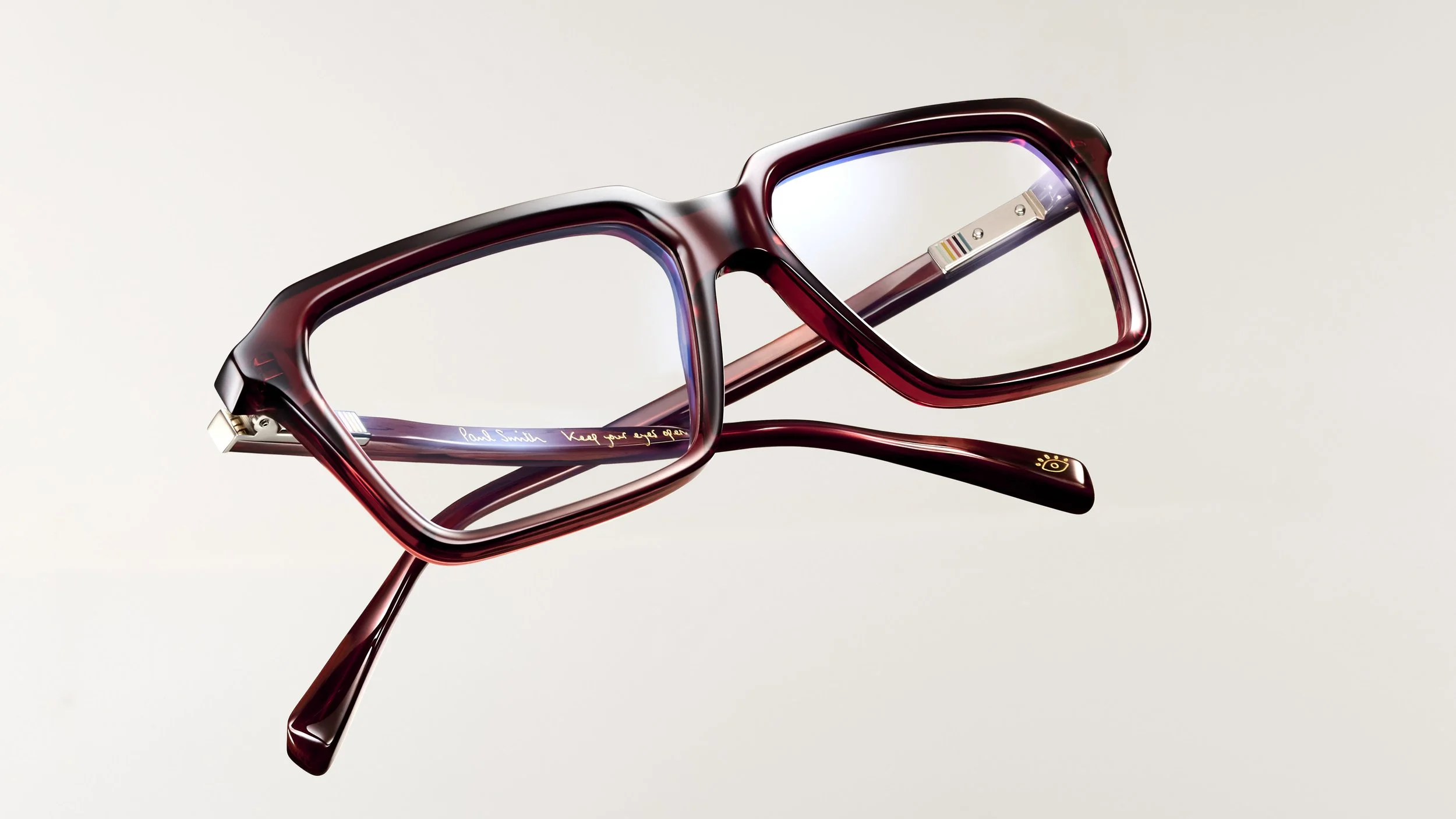 A pair of red eyeglasses with a thick frame and rectangular lenses, resting against a plain gradient background, with some inscriptions on the inside of the temples.
