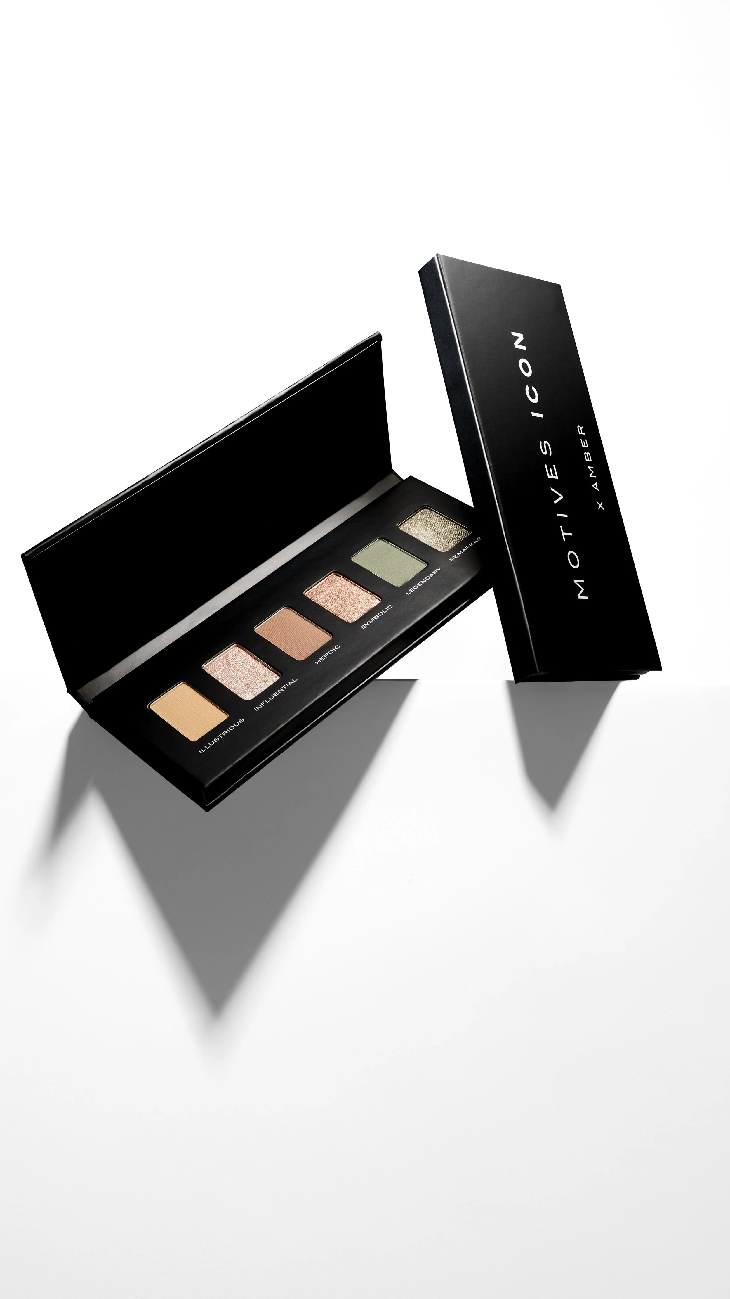 Open eyeshadow palette with six shades, labeled Illustrious, Influential, Heroic, Symbolic, Legendary, and Remarkable, with black casing and white lettering, casting shadows on a white surface.
