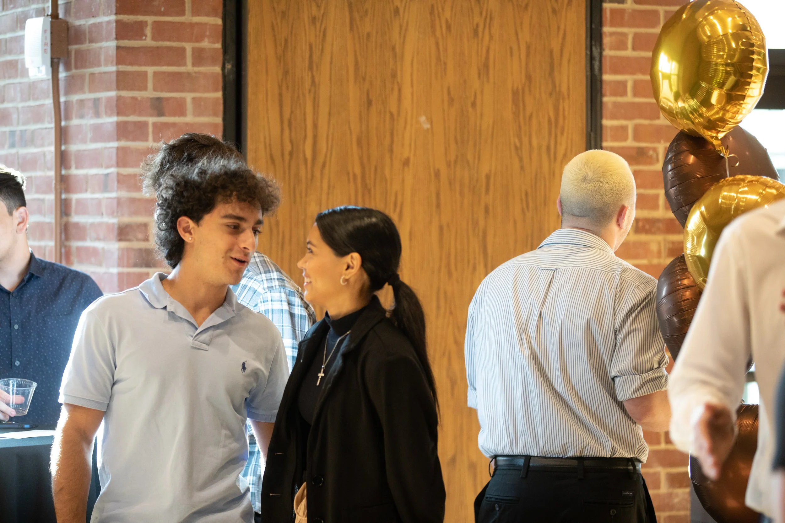 Group of people socializing at an indoor event, with balloons in the background.