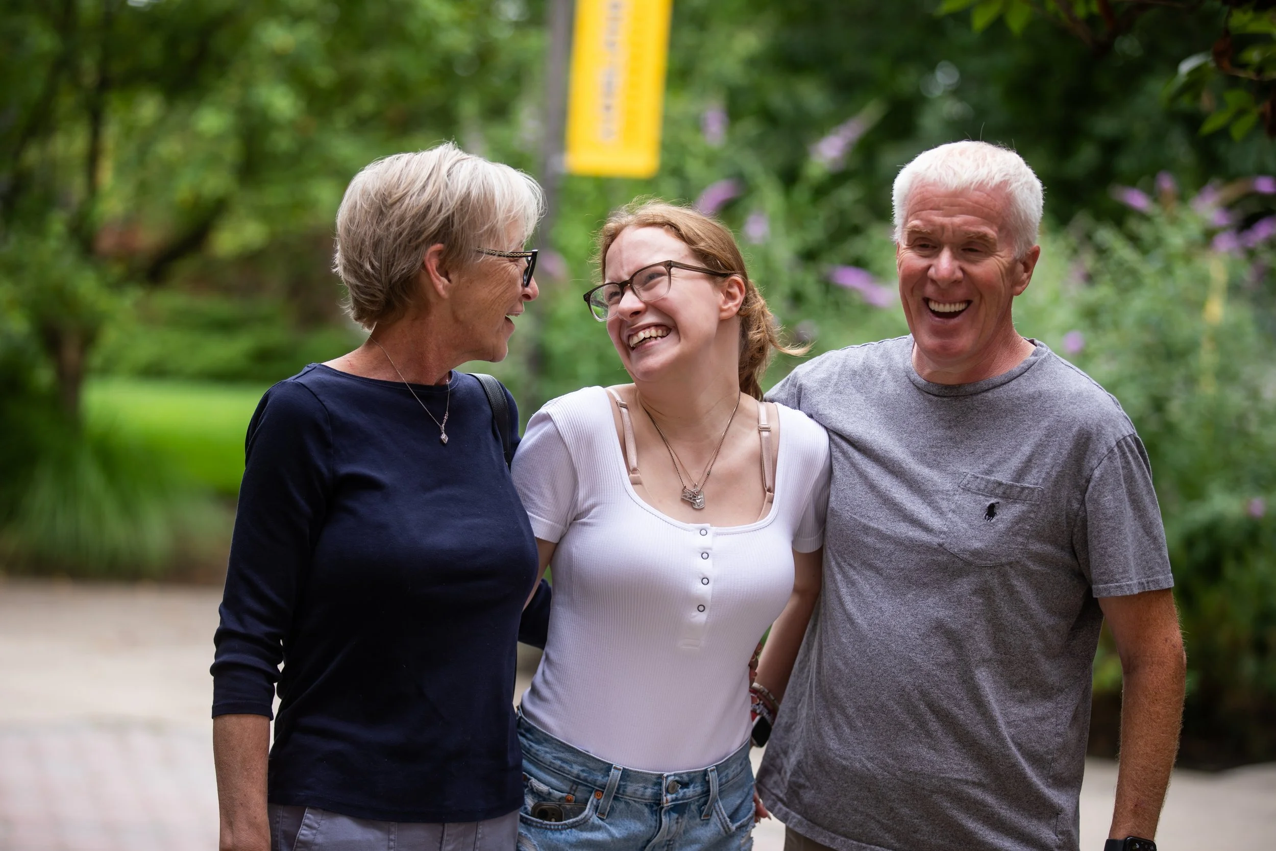 Three smiling women standing together outdoors, engaged in conversation and laughter.