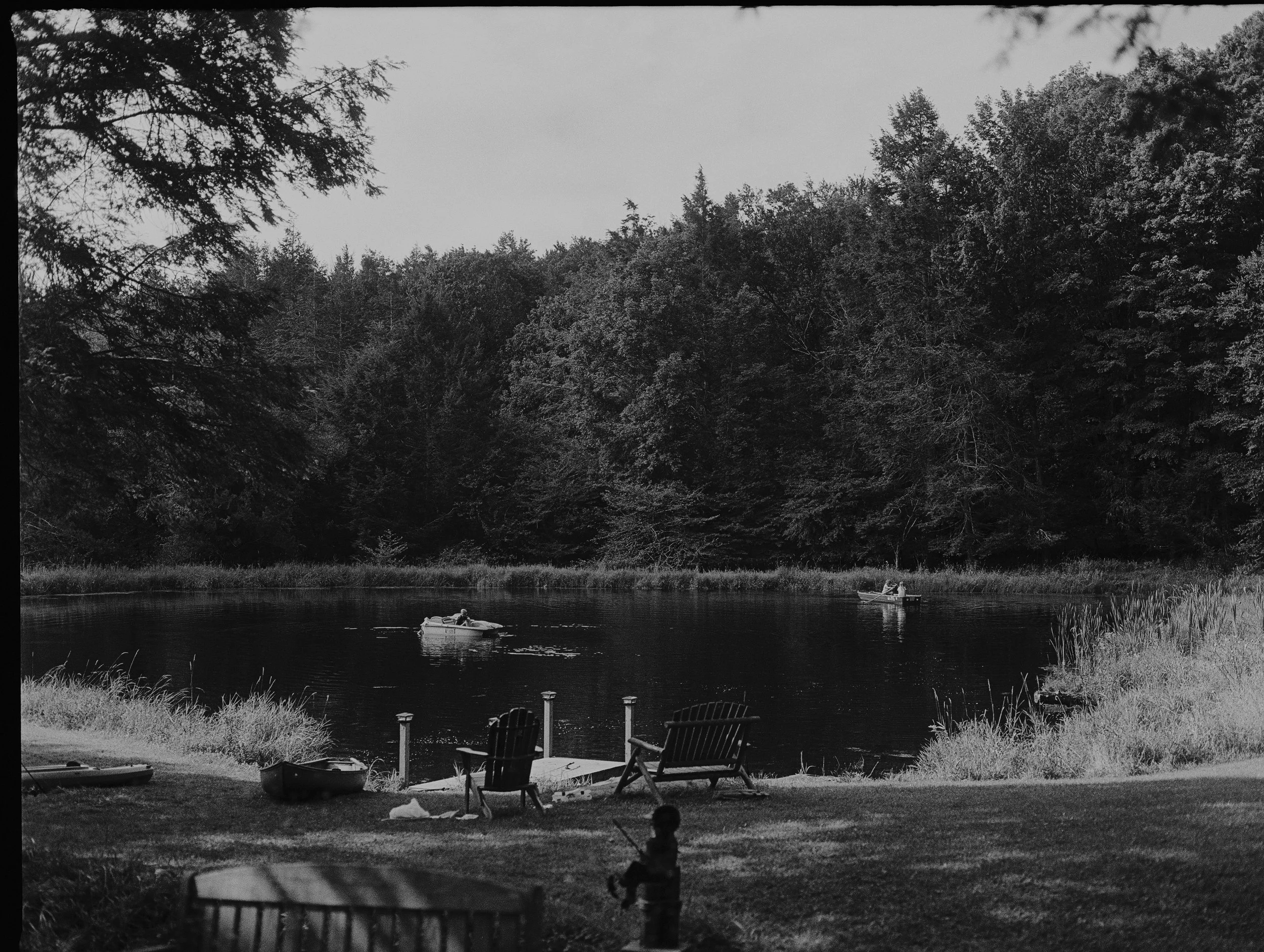 A black and white photo of a lake scene with trees in the background and a person in a small boat on the water.