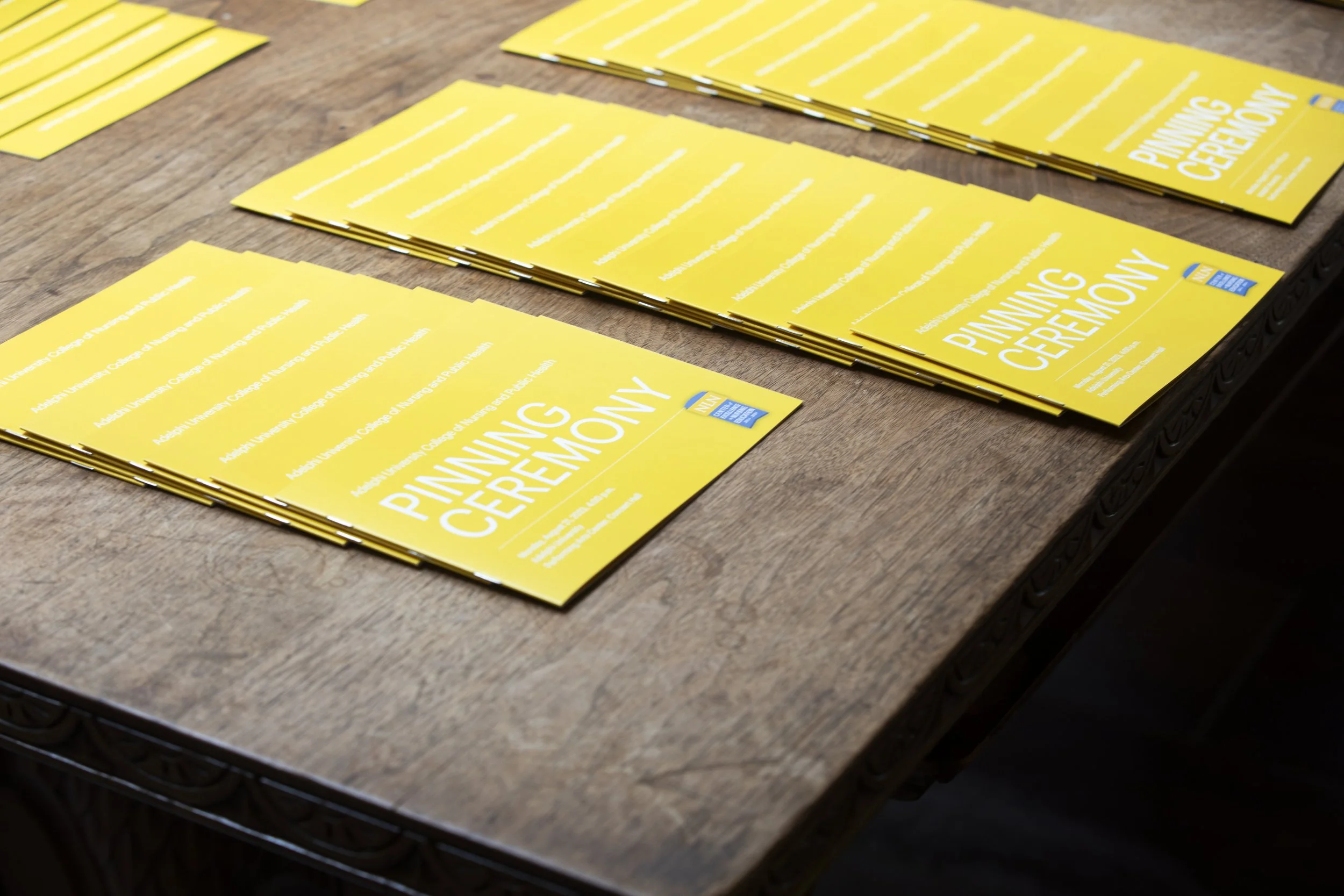 Multiple yellow brochures titled "Pinning Ceremony" are spread on a wooden table.
