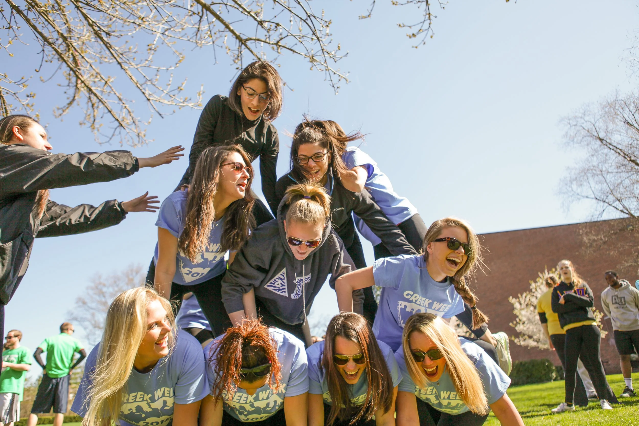 A group of young women are participating in a team activity outdoors, forming a human pyramid on a sunny day with clear skies.