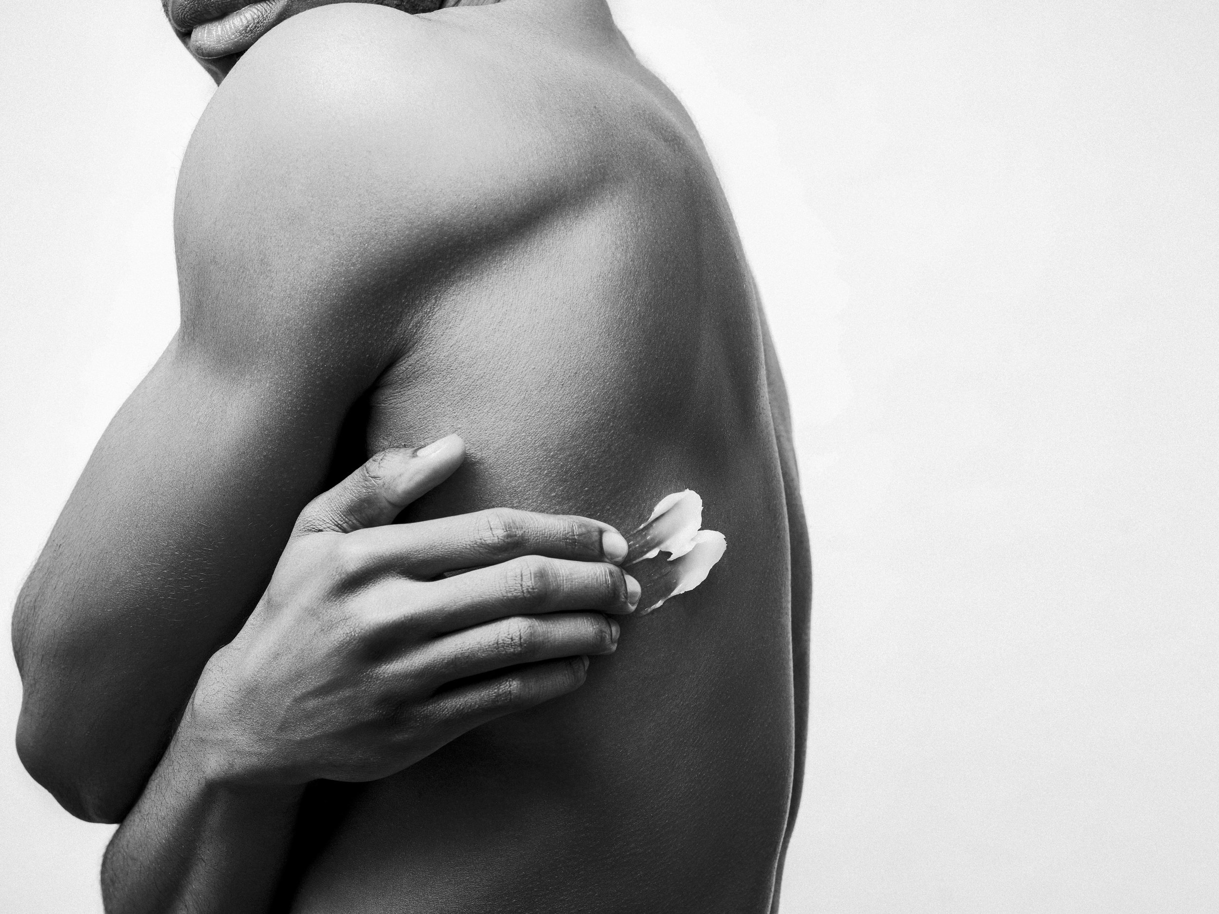 Close-up of a person's shoulder and arm, with a hand applying cream on the skin, in black and white.