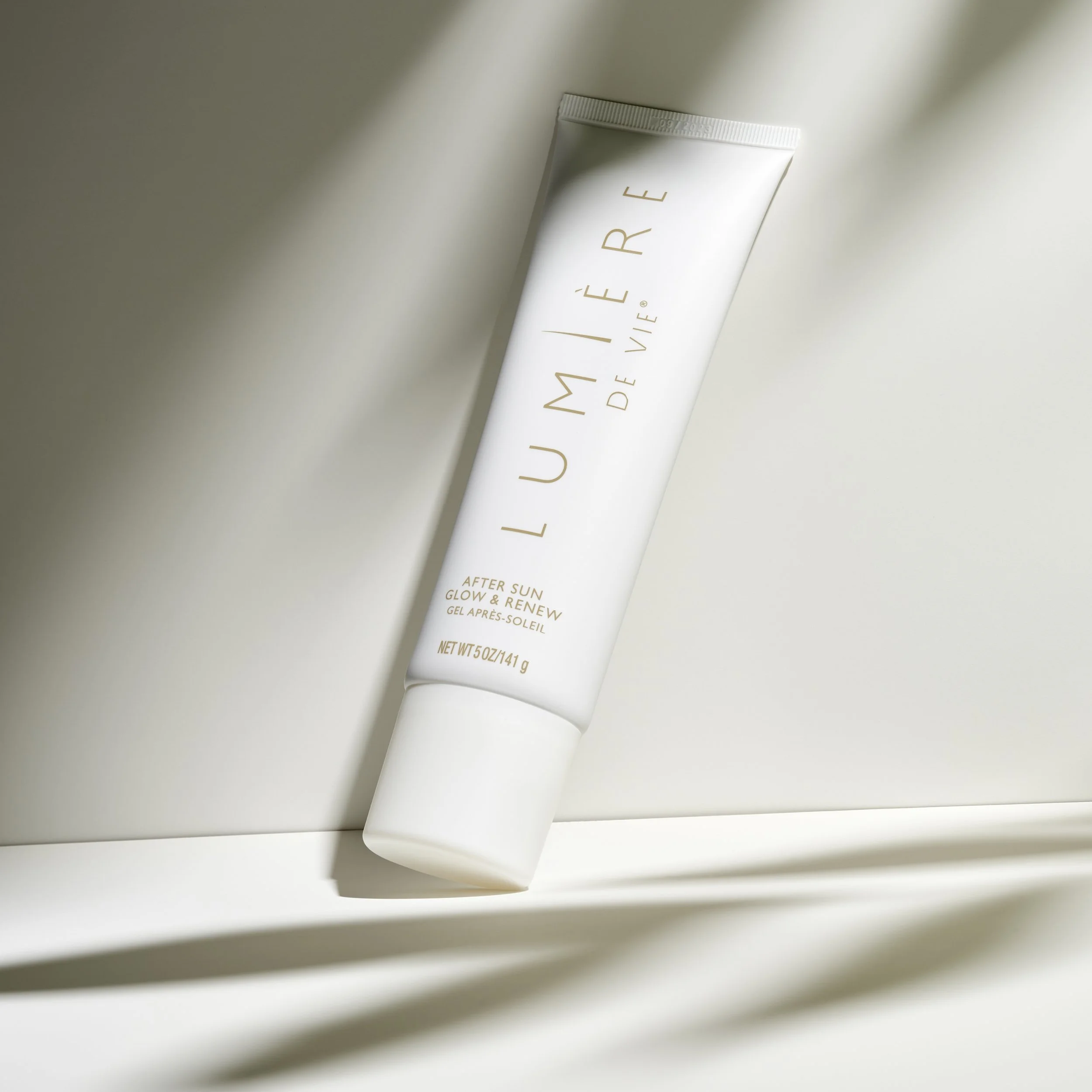 A white tube of LUMIÉRE de Vie after sun gel on a white surface with soft shadows.