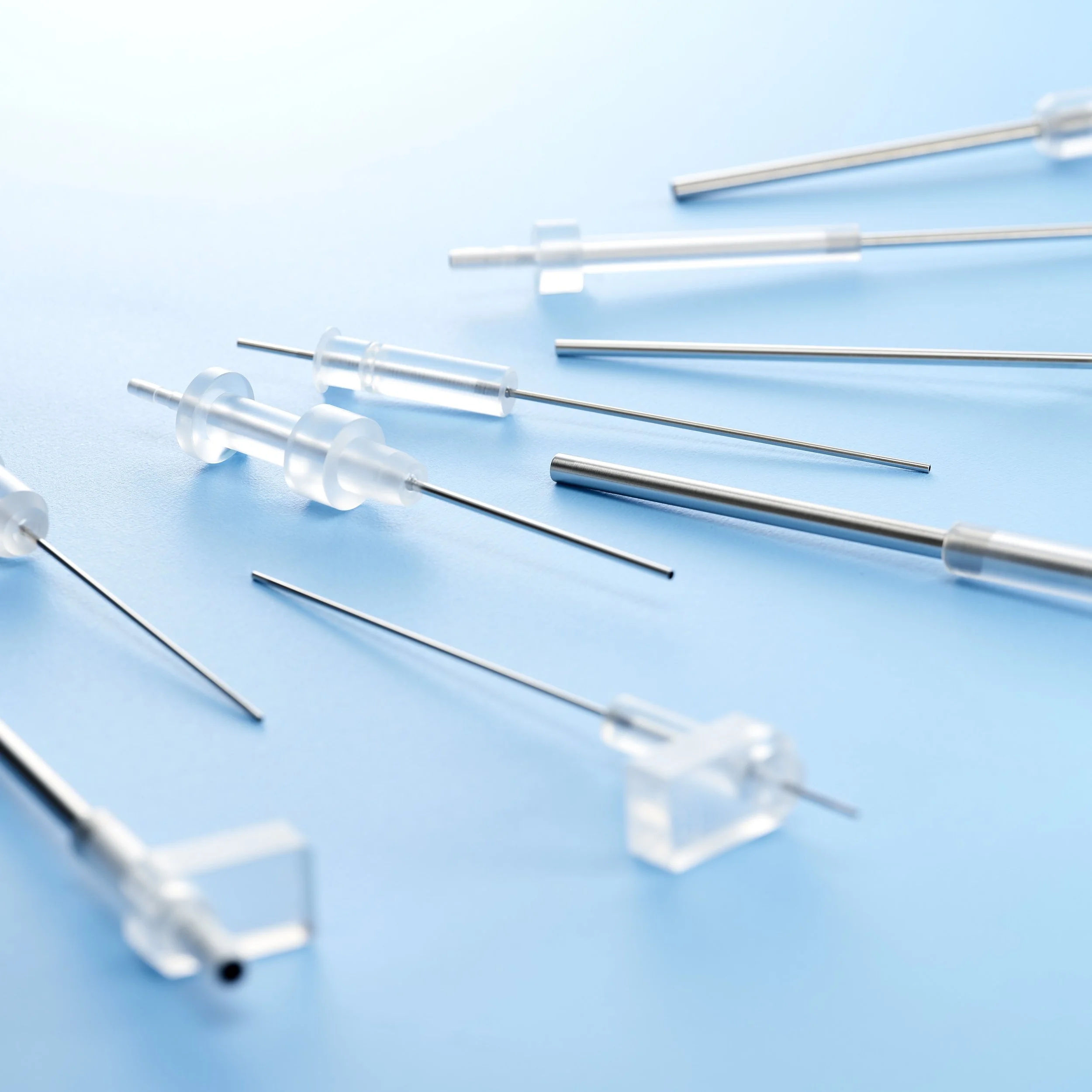 Multiple glass and metal syringes laid out on a light blue background.