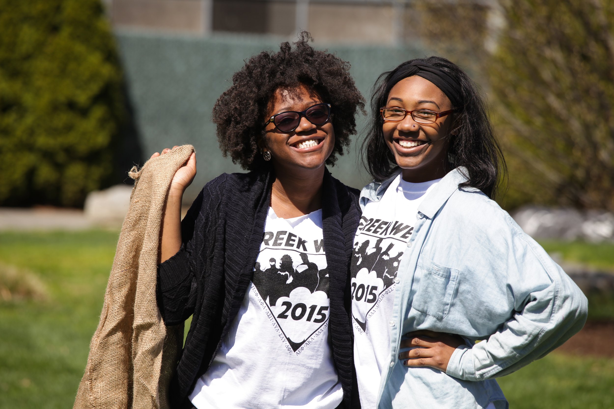 Two women smiling outdoors, wearing matching event T-shirts, with trees and grass in the background.
