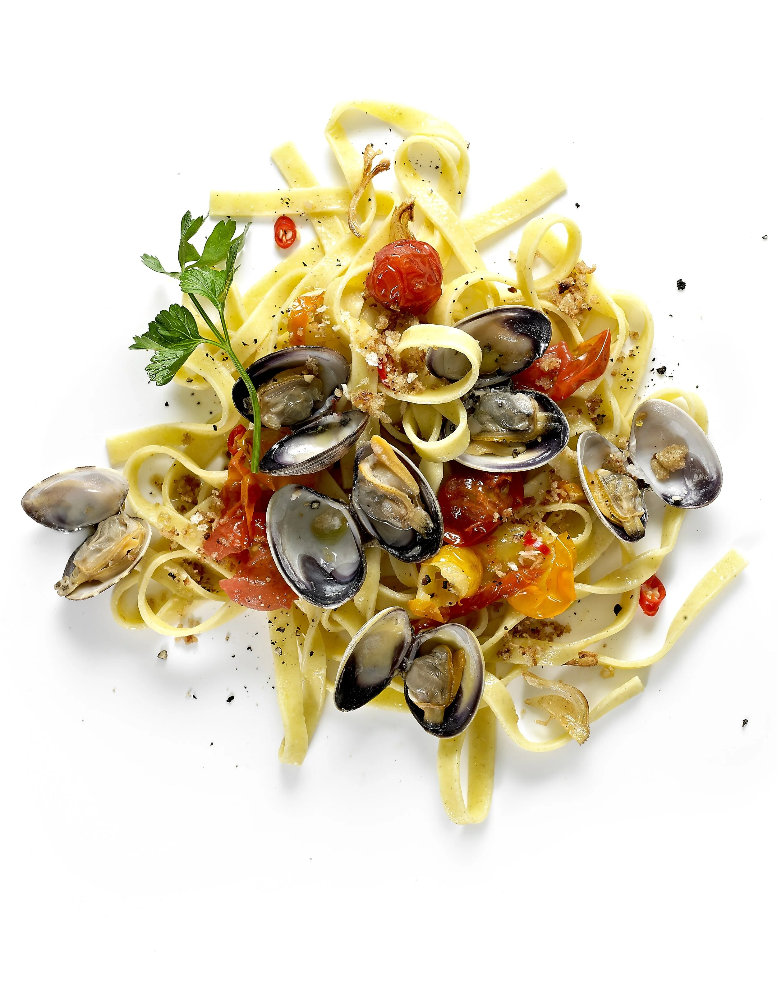 A plate of seafood pasta with linguine, cherry tomatoes, clams, mussels, garnished with black pepper and fresh parsley