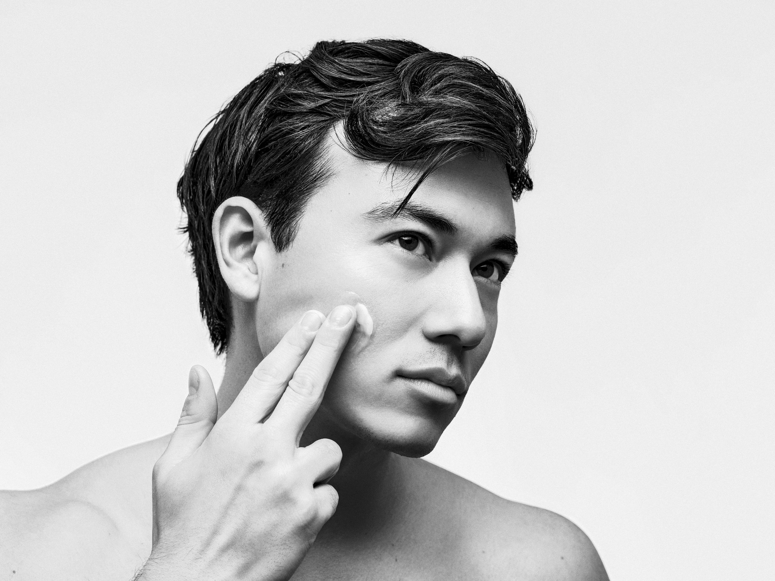Black and white close-up portrait of a young man with dark hair touching his cheek with two fingers.