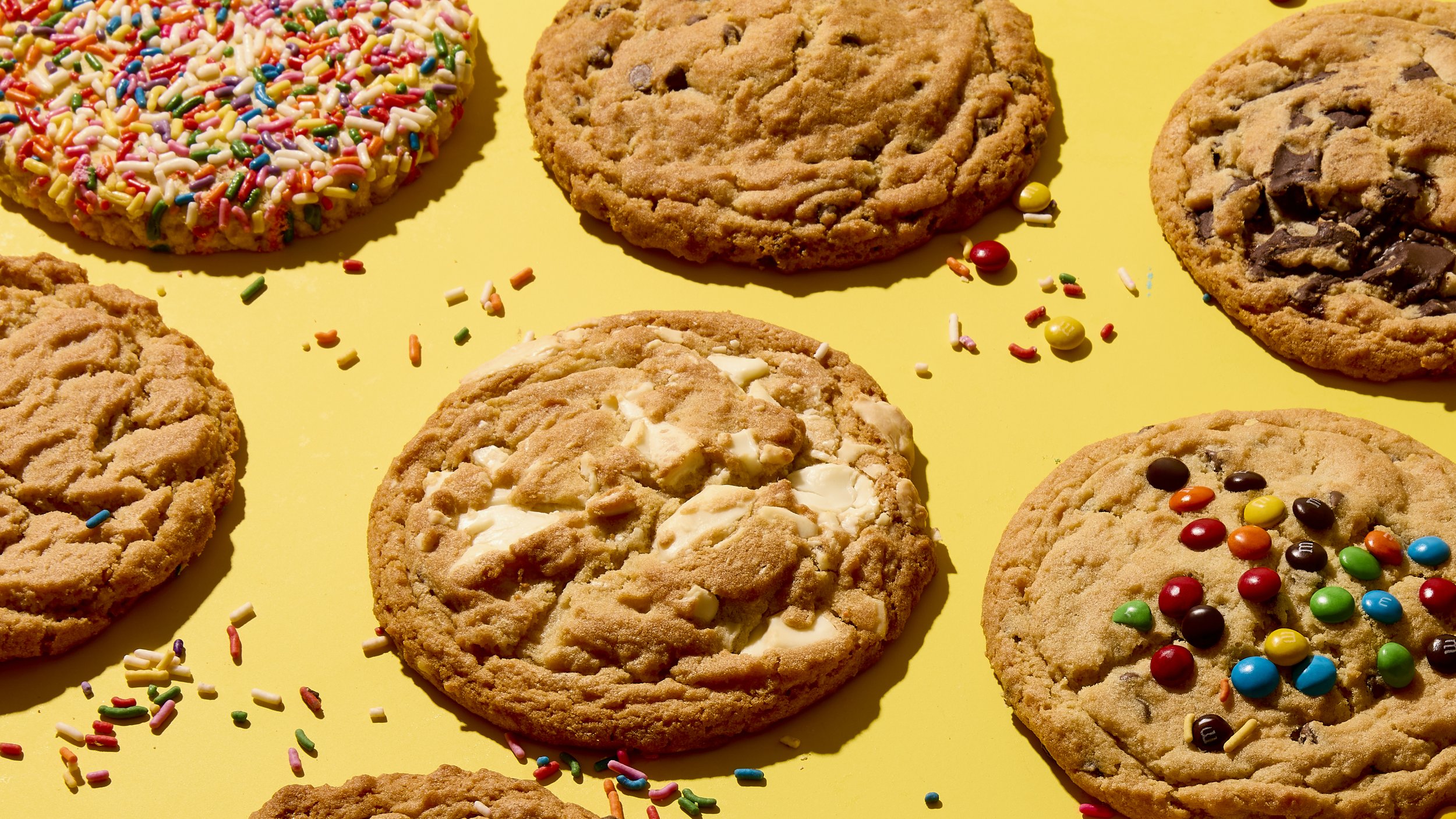 Assorted cookies with sprinkles and chocolate chips on a yellow background.