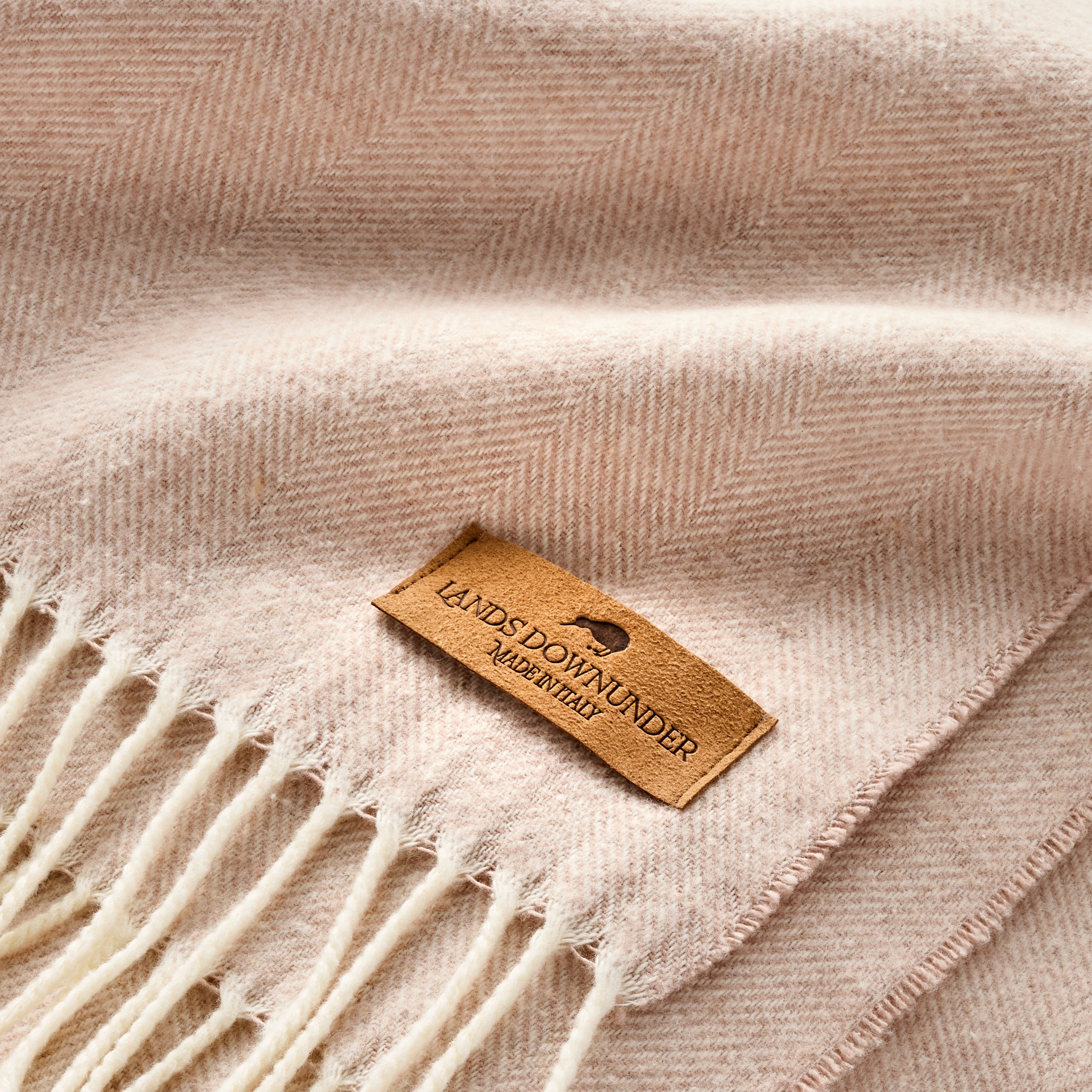 Close-up of beige fabric with white diagonal stripes and a small, rectangular, light brown tag that reads "LANDS DOWN UNDER MADE IN ITALY."