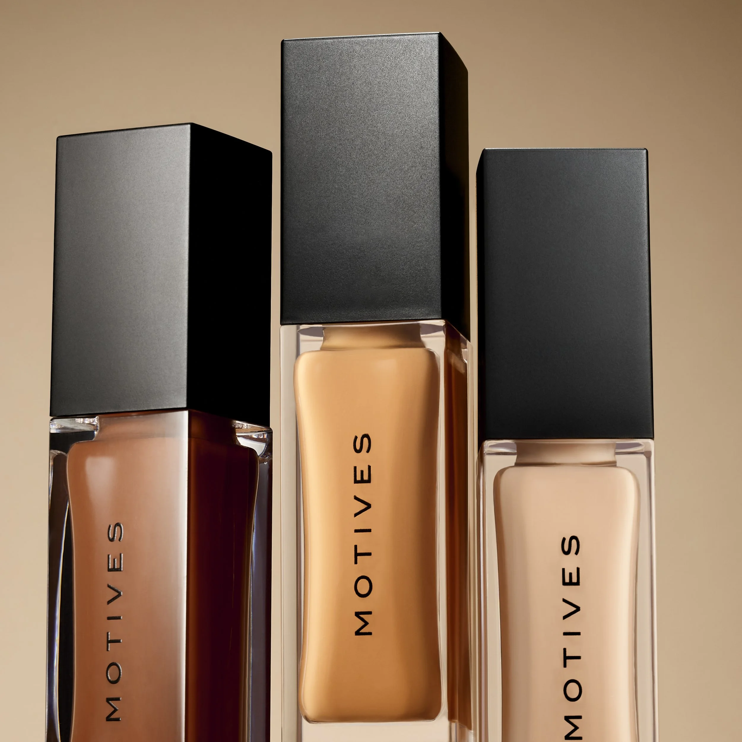 Three bottles of MOTIVIES foundation with black caps, arranged in a row against a neutral background.