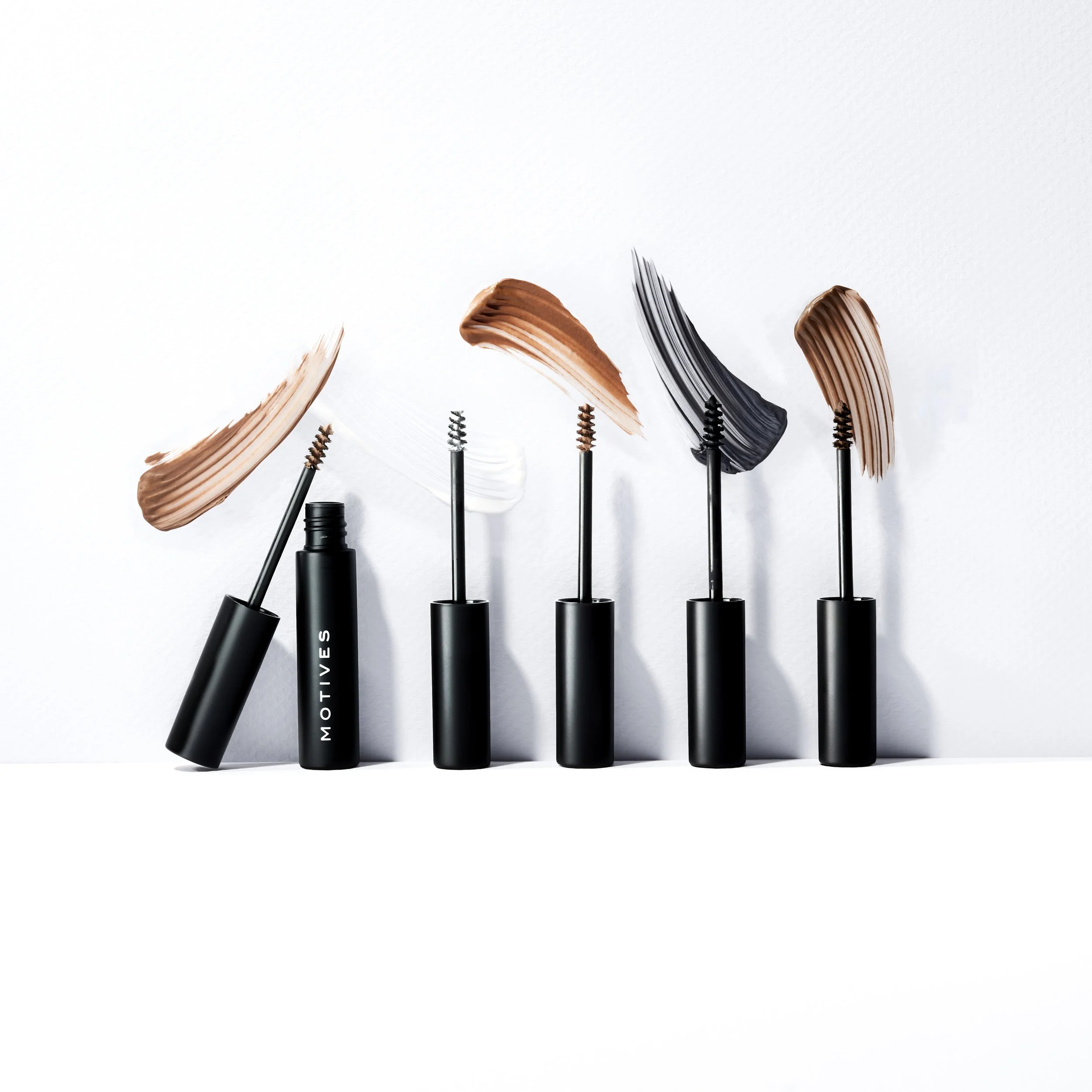Five mascara tubes with brushes, each with different shades of mascara, arranged in a row on a white background.