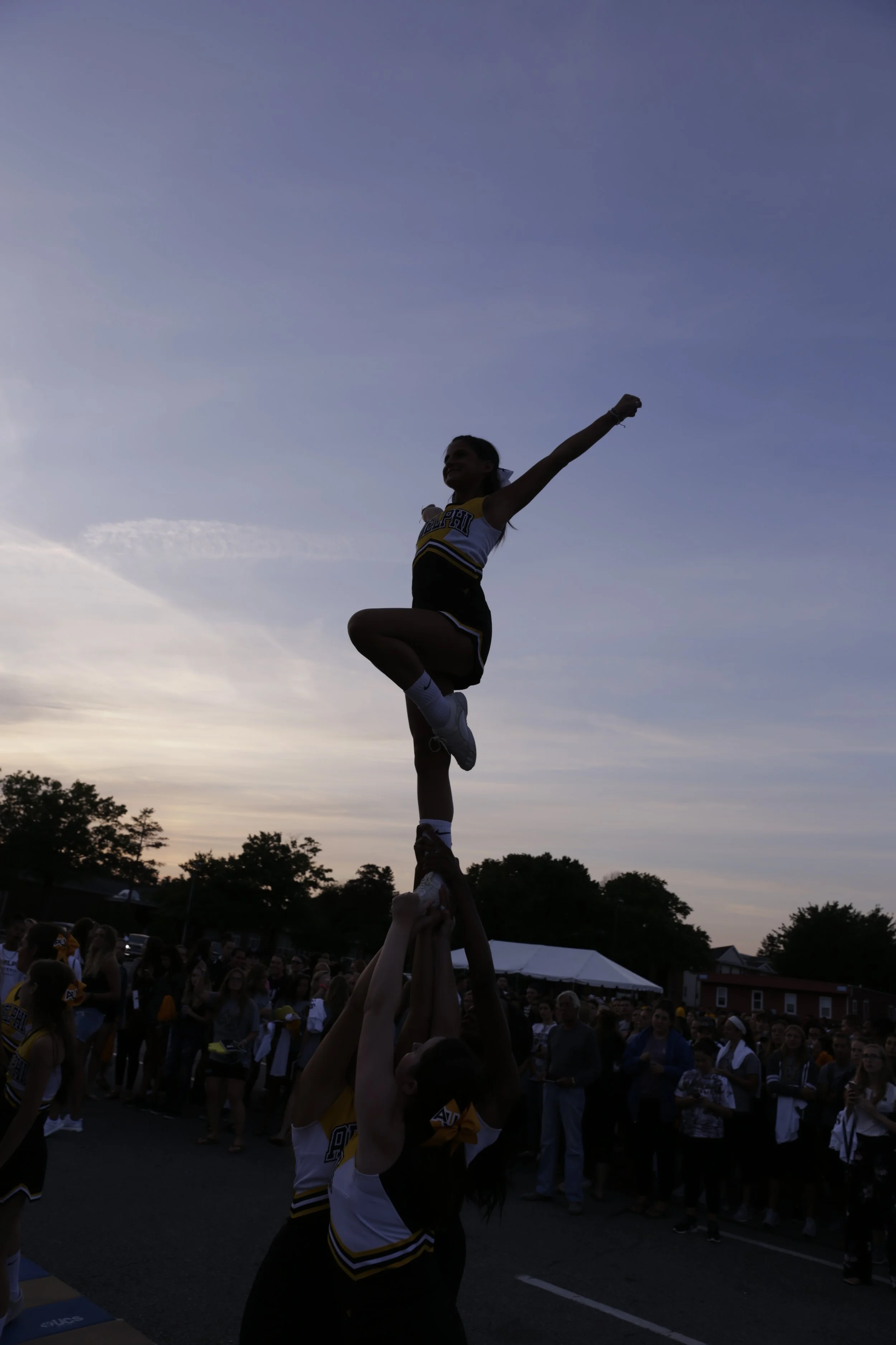Cheerleader building a human pyramid during an outdoor event at sunset.