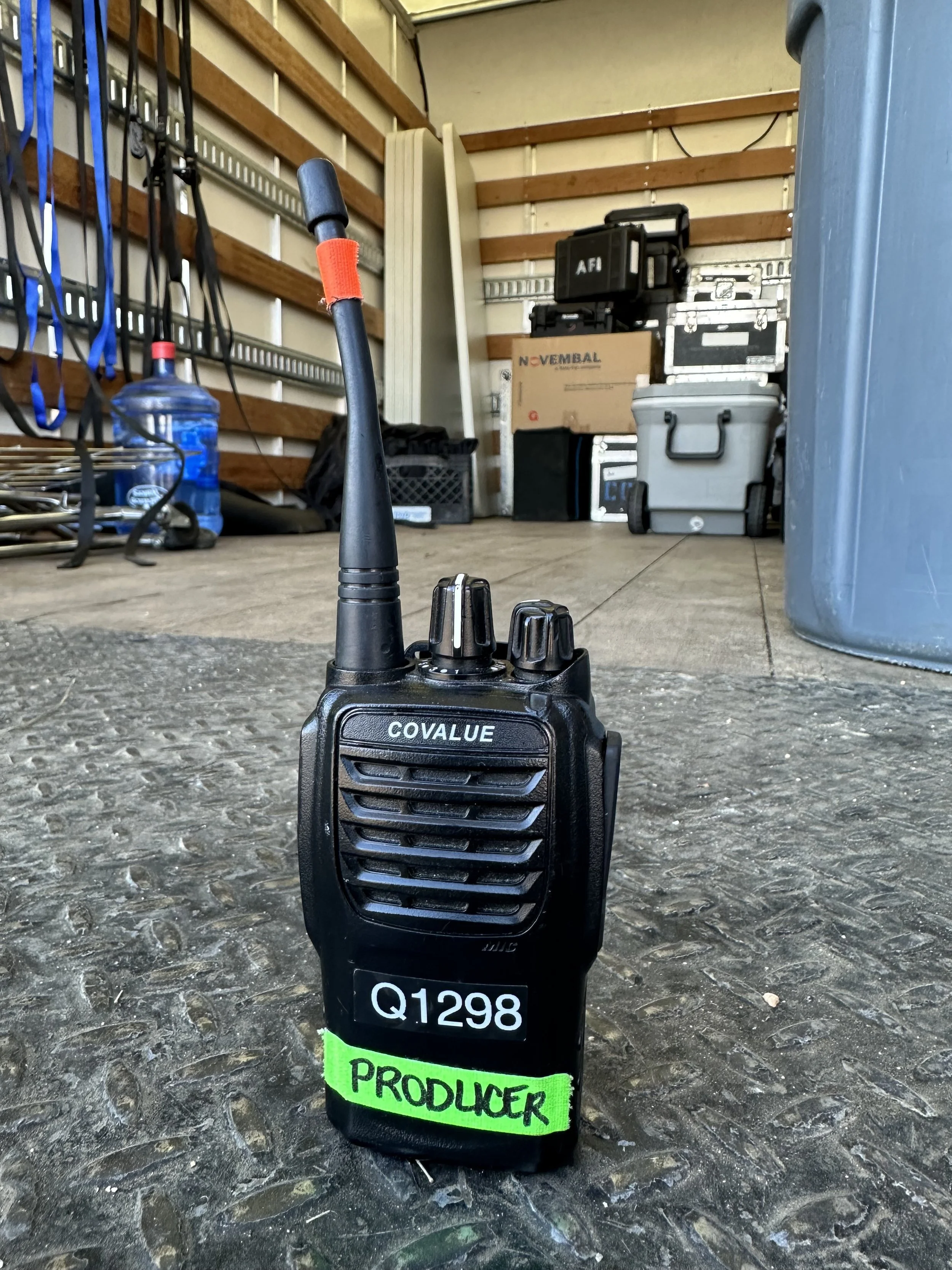 Black two-way radio walkie-talkie labeled 'PRODUCER' with green tape at the bottom, on a garage floor.