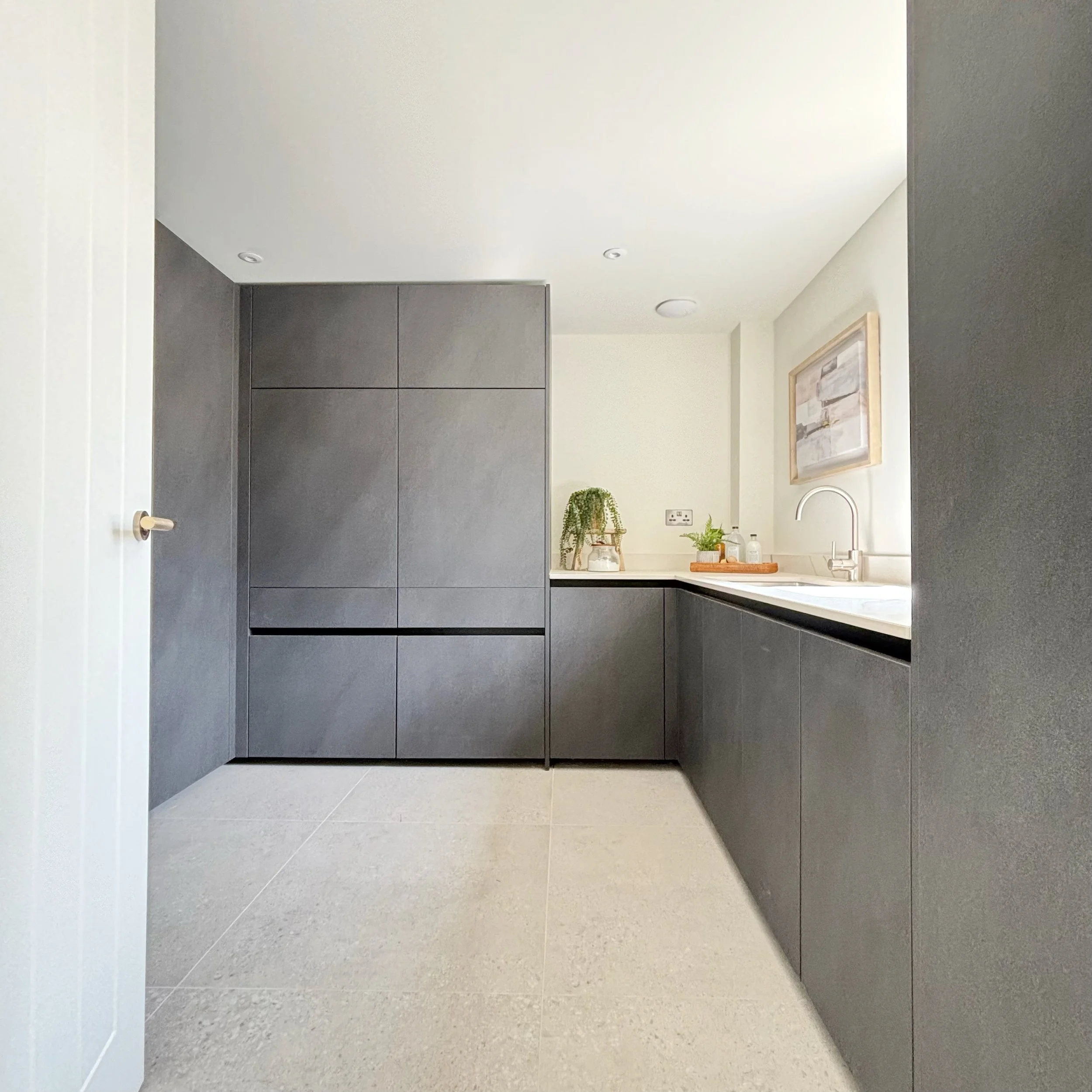 Utility room in carbon coloured stone effect cabinets, washing machine and tumble dryer off floor inside cabinets