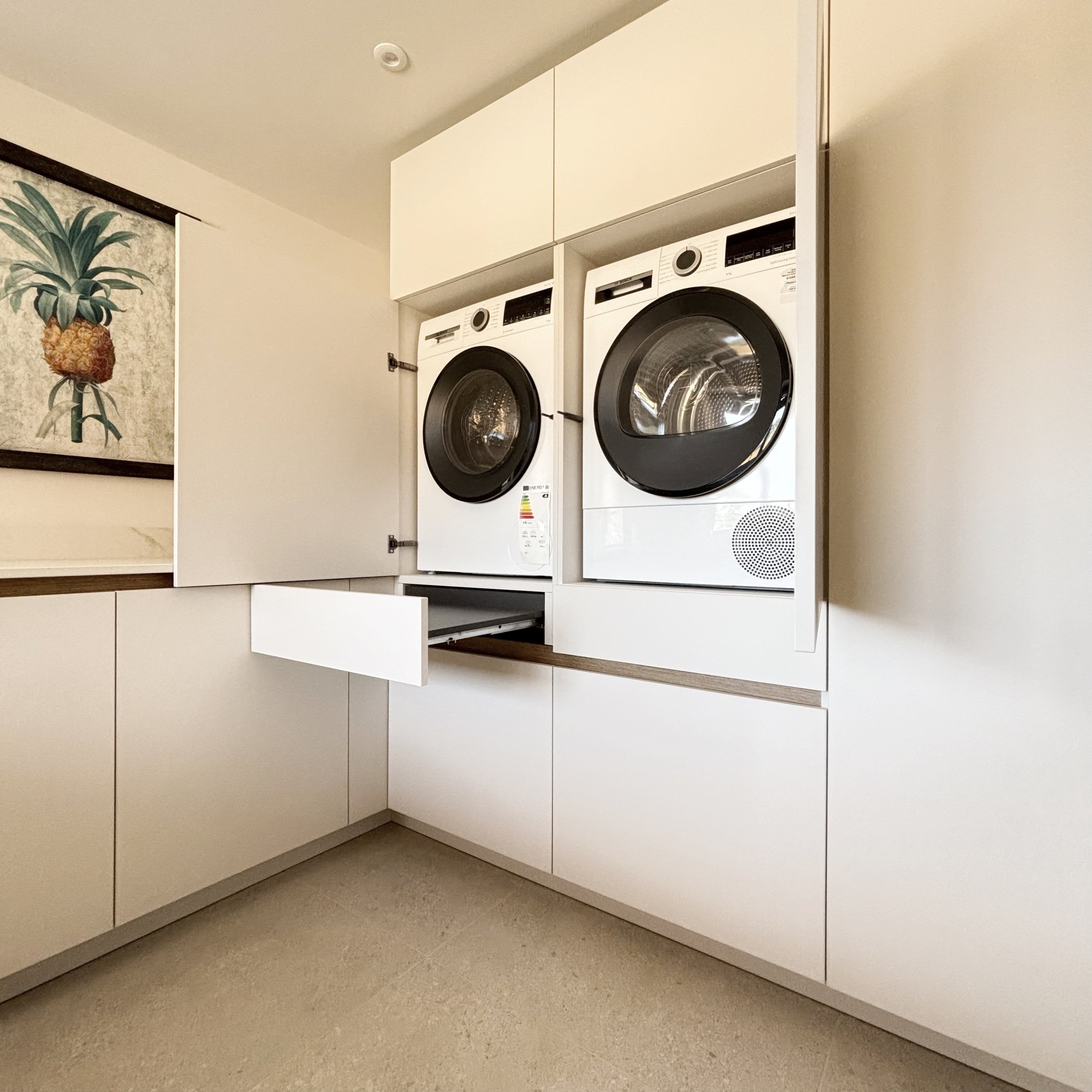 A laundry area with a front-loading washer and dryer set, built into white cabinetry with doors to hide the appliances.
