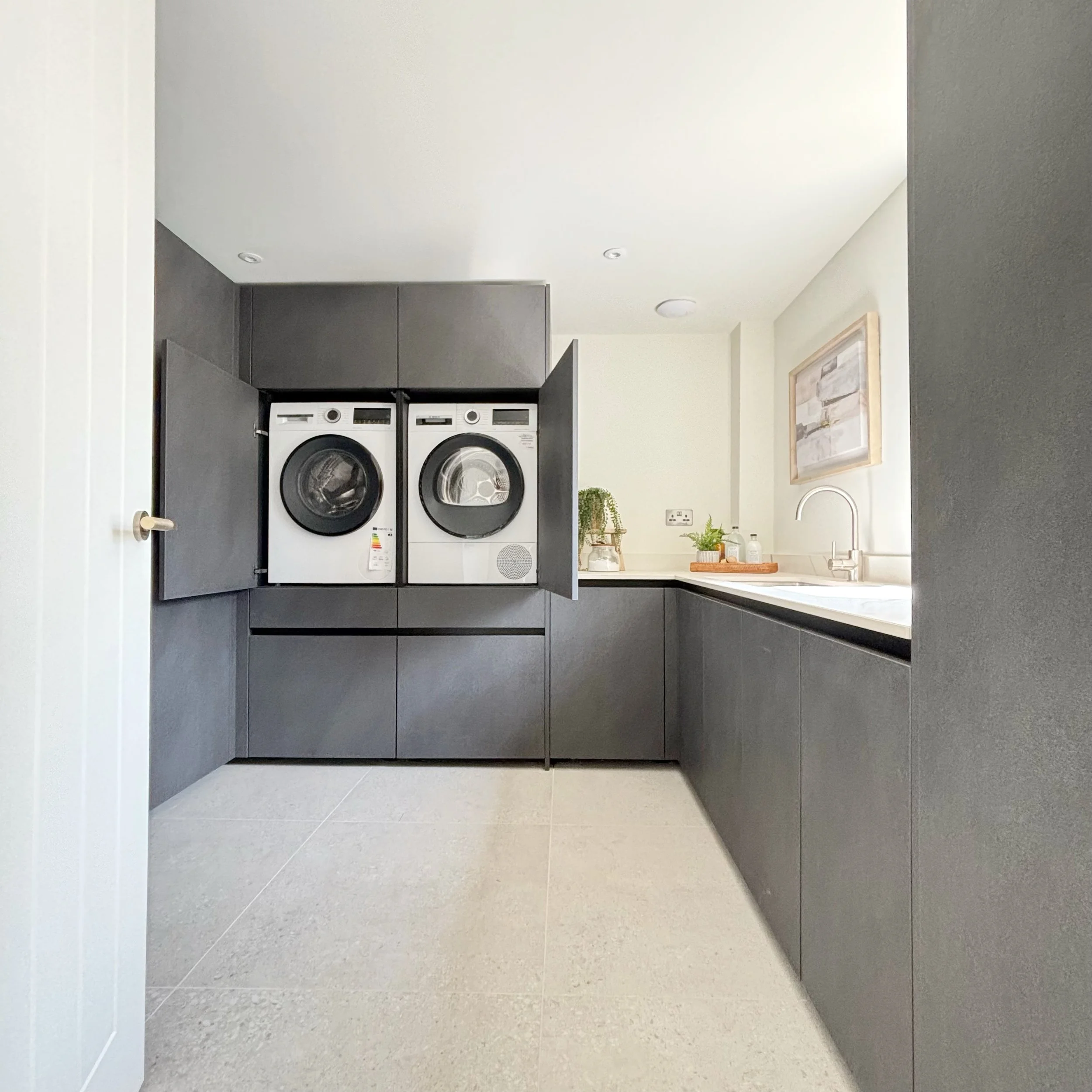 Utility room in carbon coloured stone effect cabinets, washing machine and tumble dryer off floor inside cabinets